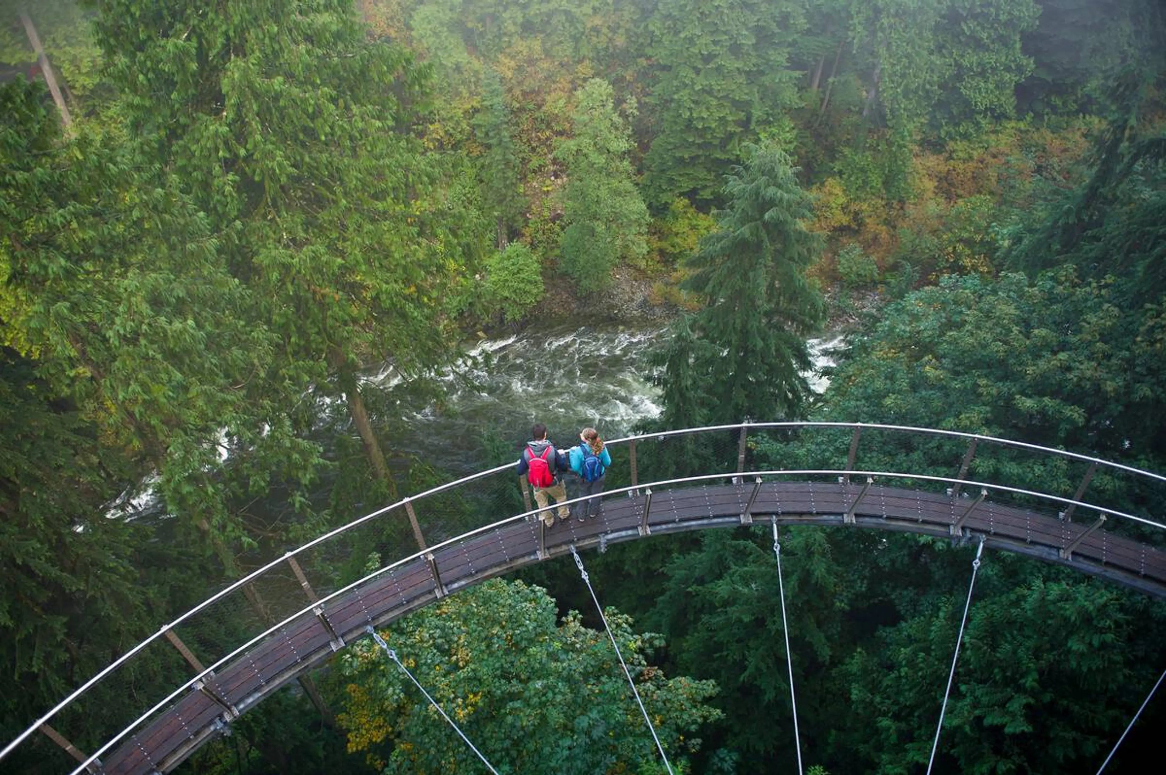 Two people wearing rain jackets enjoy the Capilano Suspension Bridge in Vancouver