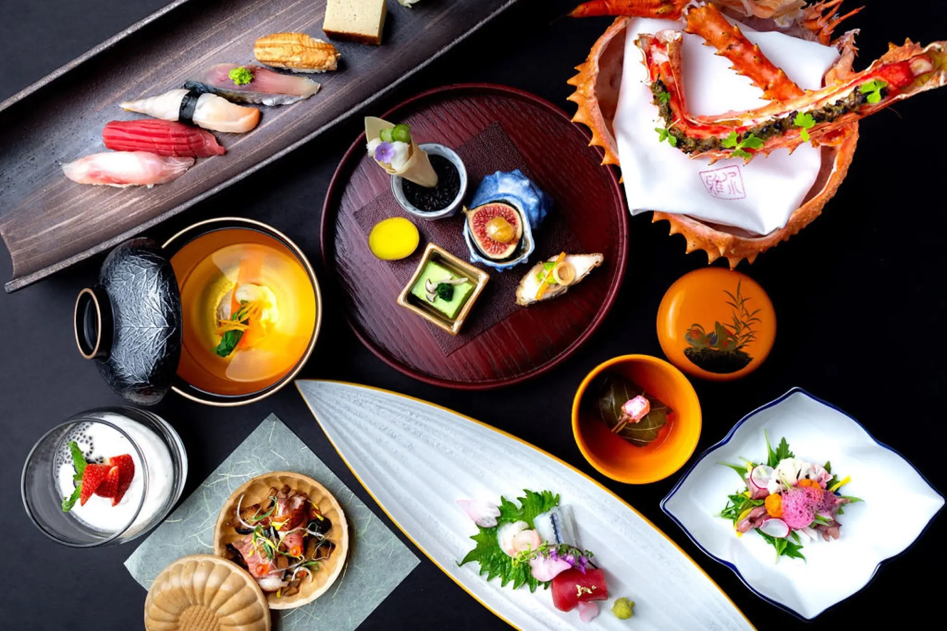 Assorted Japanese dishes including sushi, sashimi, crab legs, and various small plated appetizers on black and white plates.