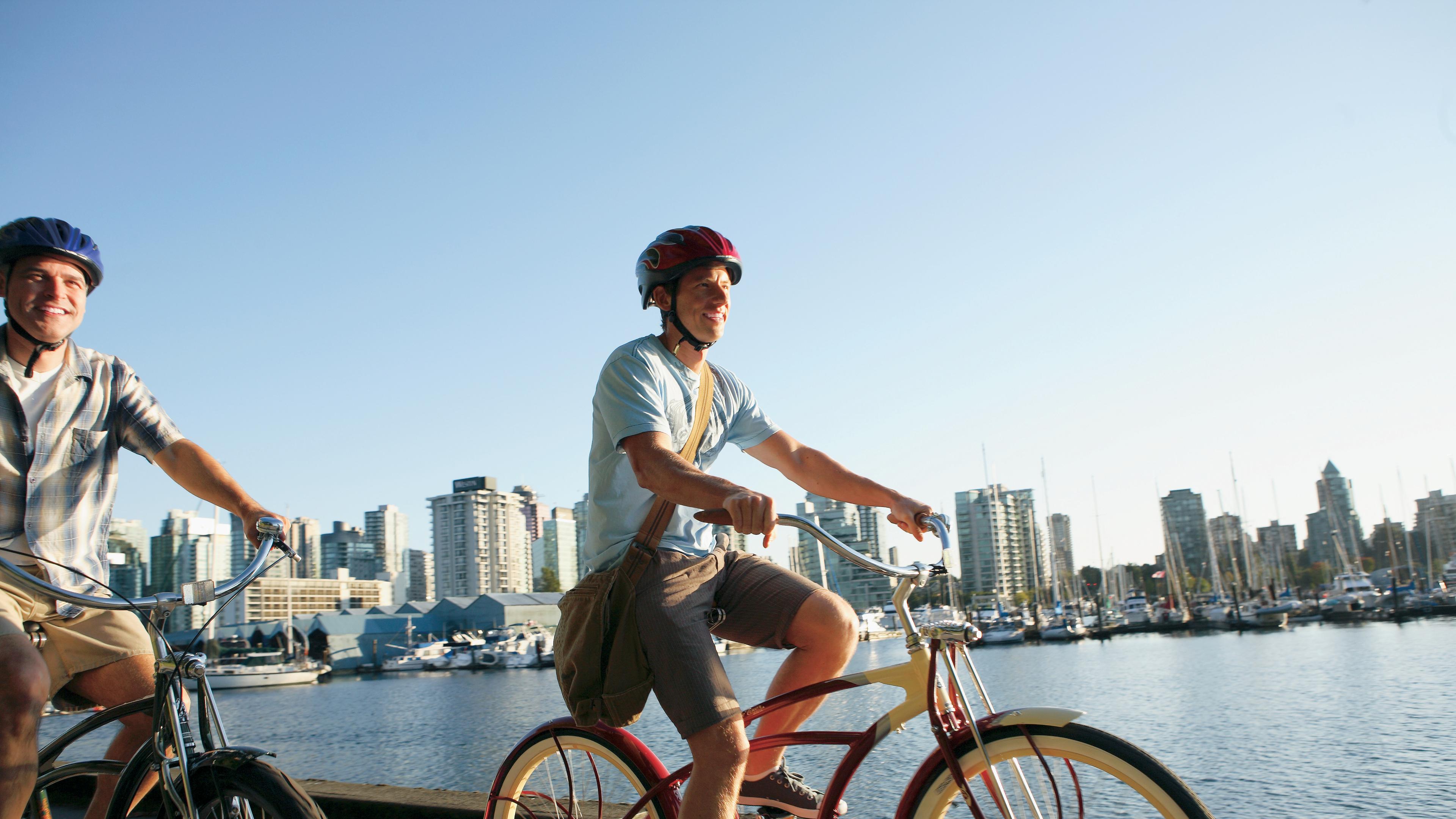 Two people ride bikes on the Seawall in front of the city skyline