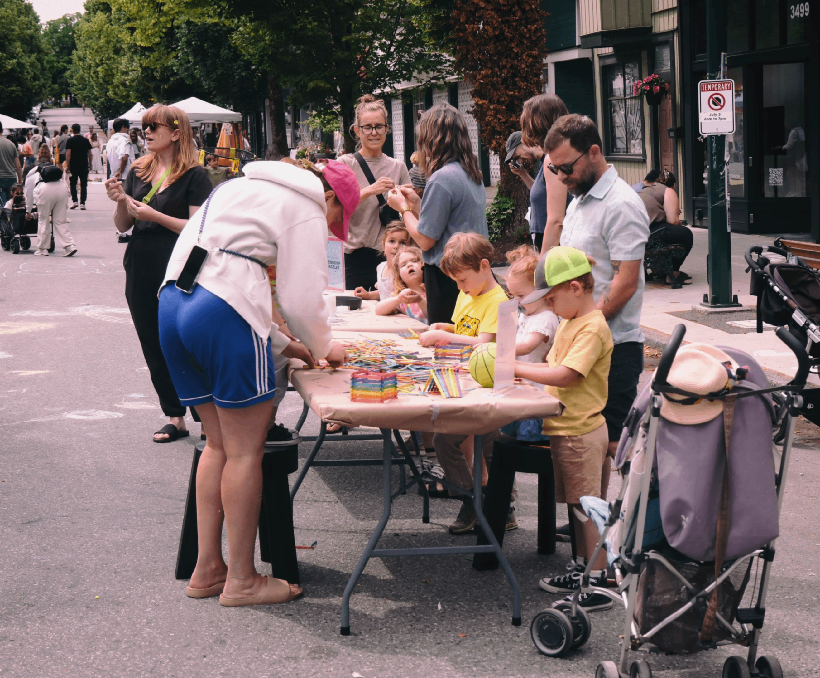 Children and adults gathered around a table outdoors, engaging in arts and crafts with colored pencils and paper.