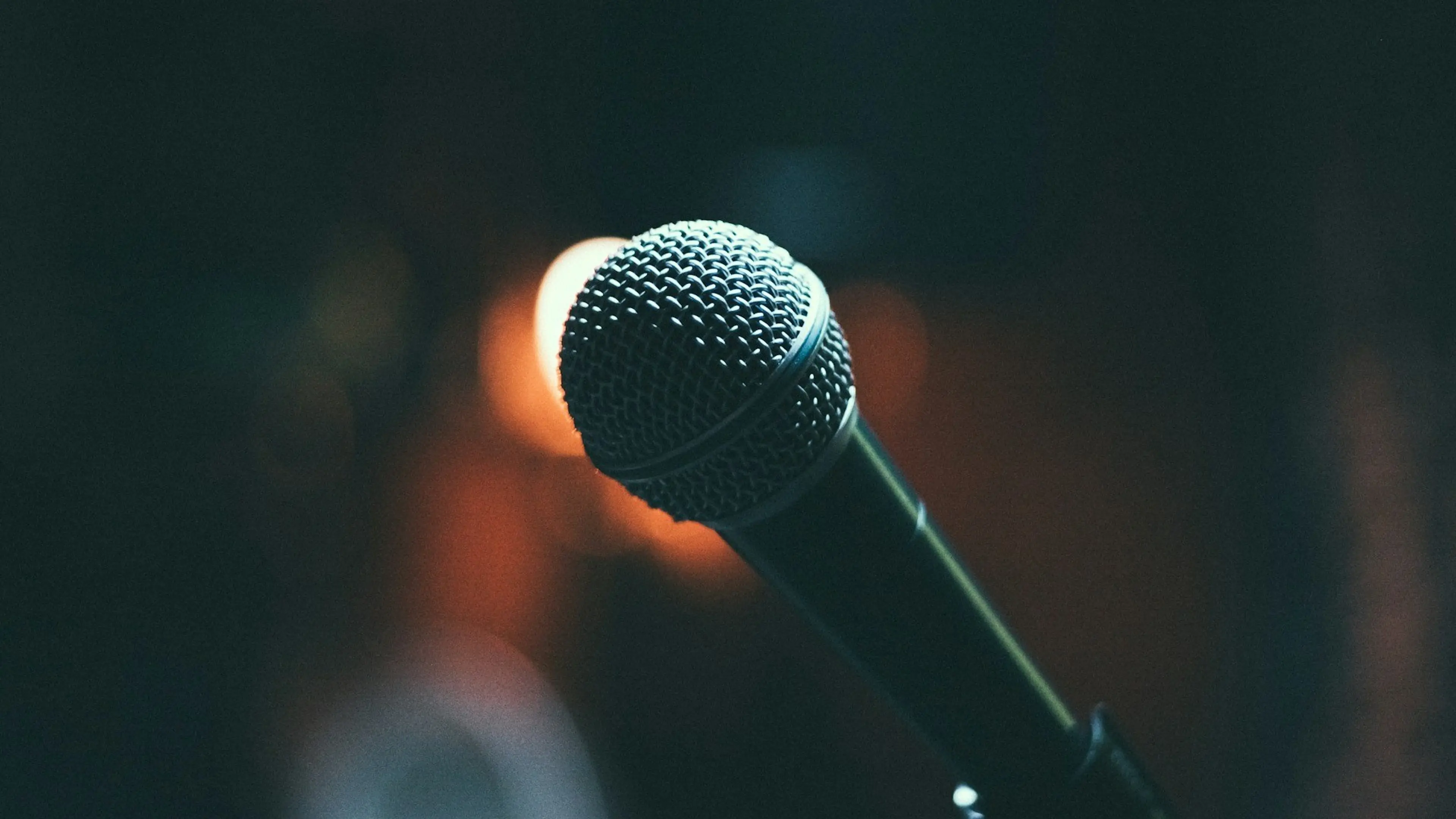 Close-up of a microphone with a blurred dark background and warm light bokeh.