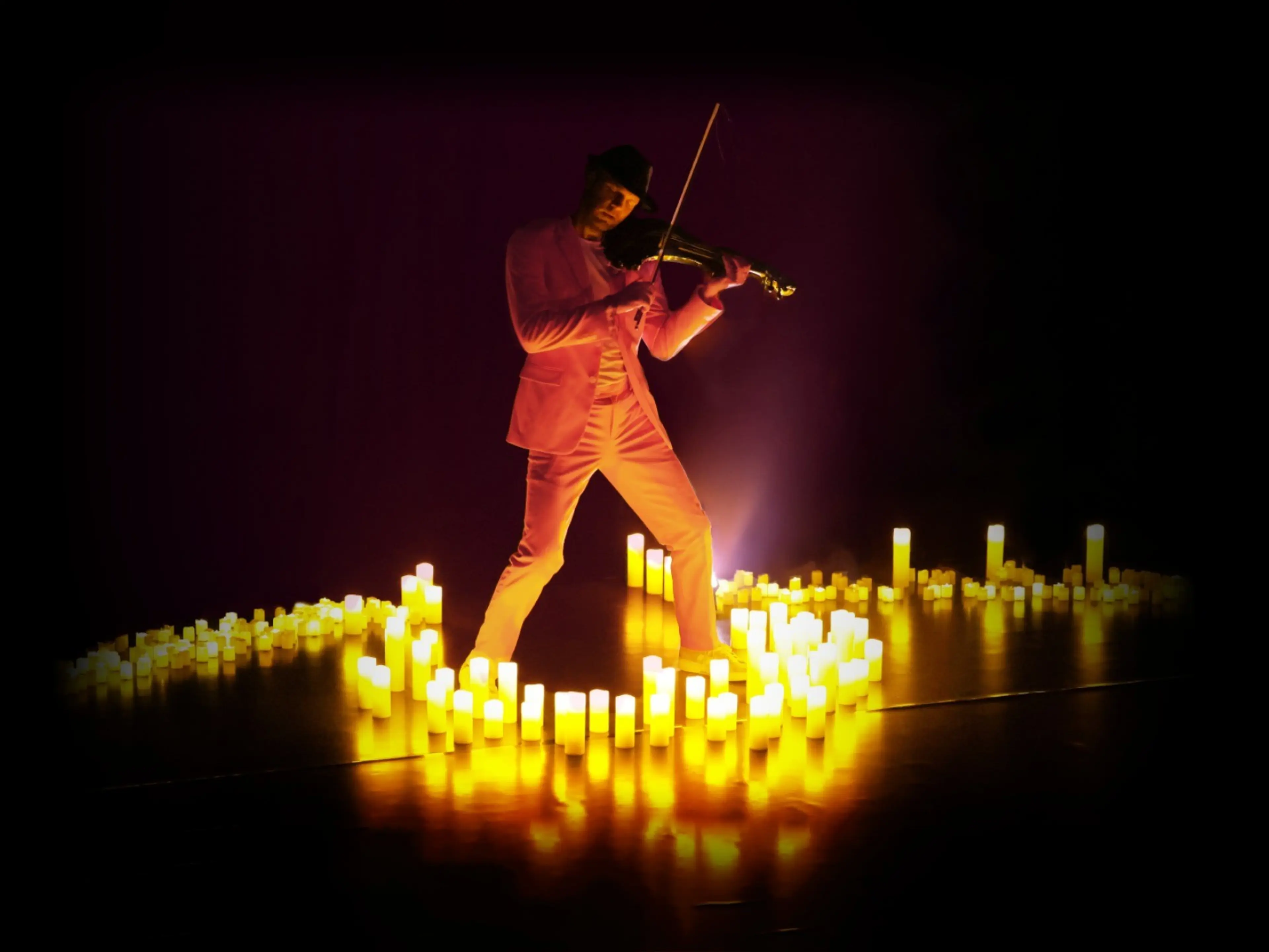 Person in pink suit playing violin surrounded by glowing yellow candles in a dark setting.