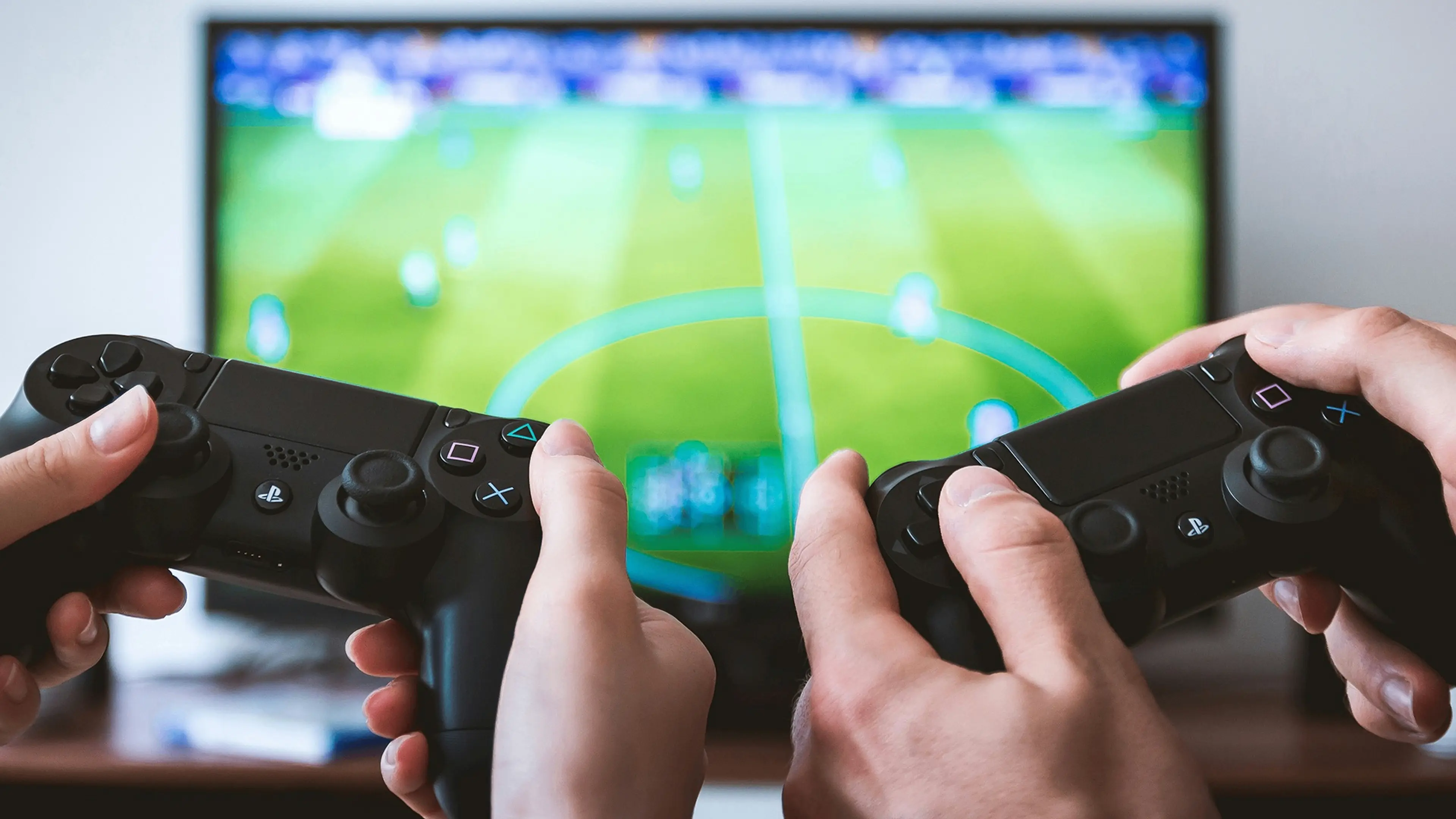Two people holding black PlayStation controllers playing a soccer video game on a TV screen.