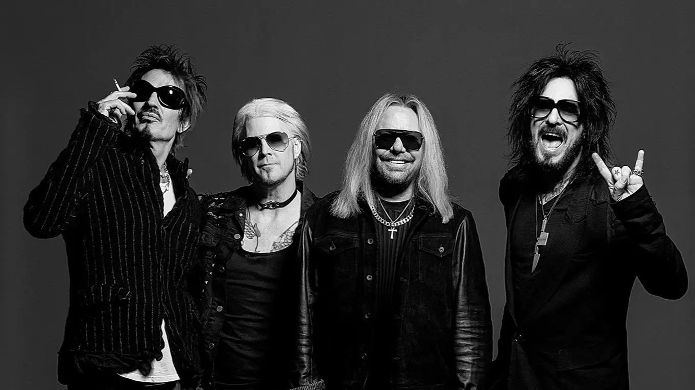 Four people wearing sunglasses and dark clothing posing against a plain dark background, one holding a cigarette and another making a rock hand gesture.