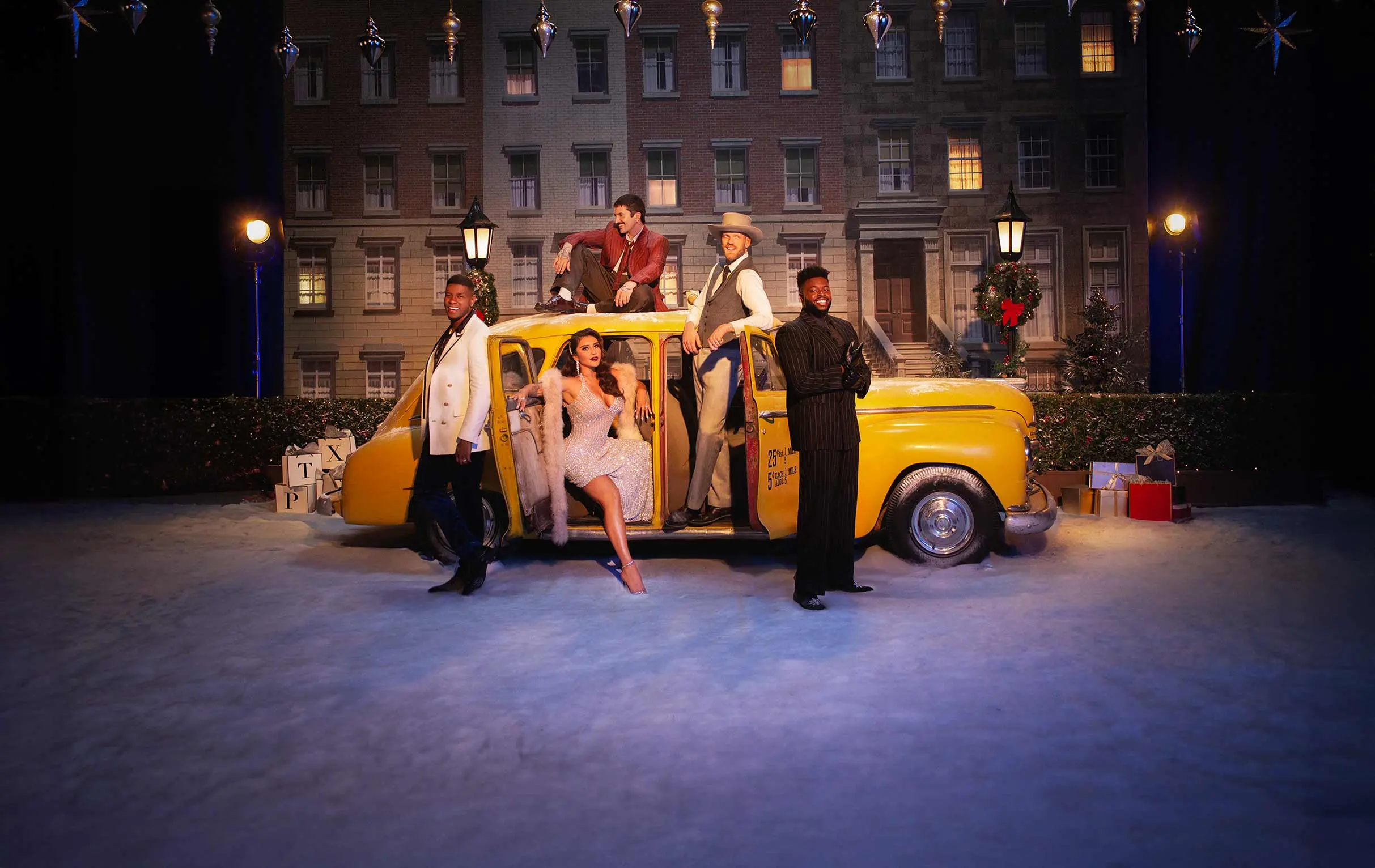 Five people posing with a yellow vintage taxi in front of a building backdrop decorated with Christmas wreaths and gifts.
