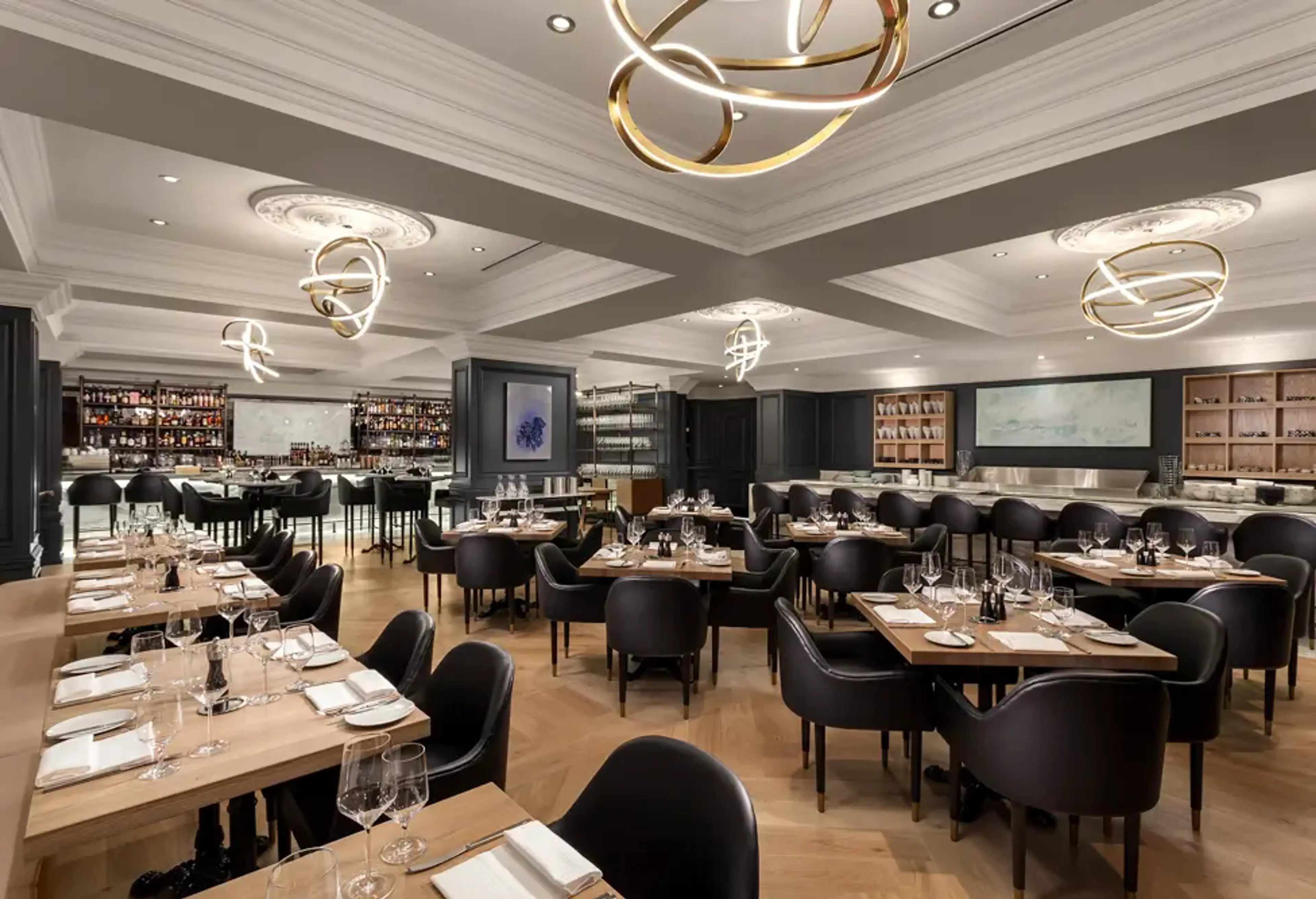 Modern restaurant interior with wooden tables, black chairs, and artistic circular ceiling lights.