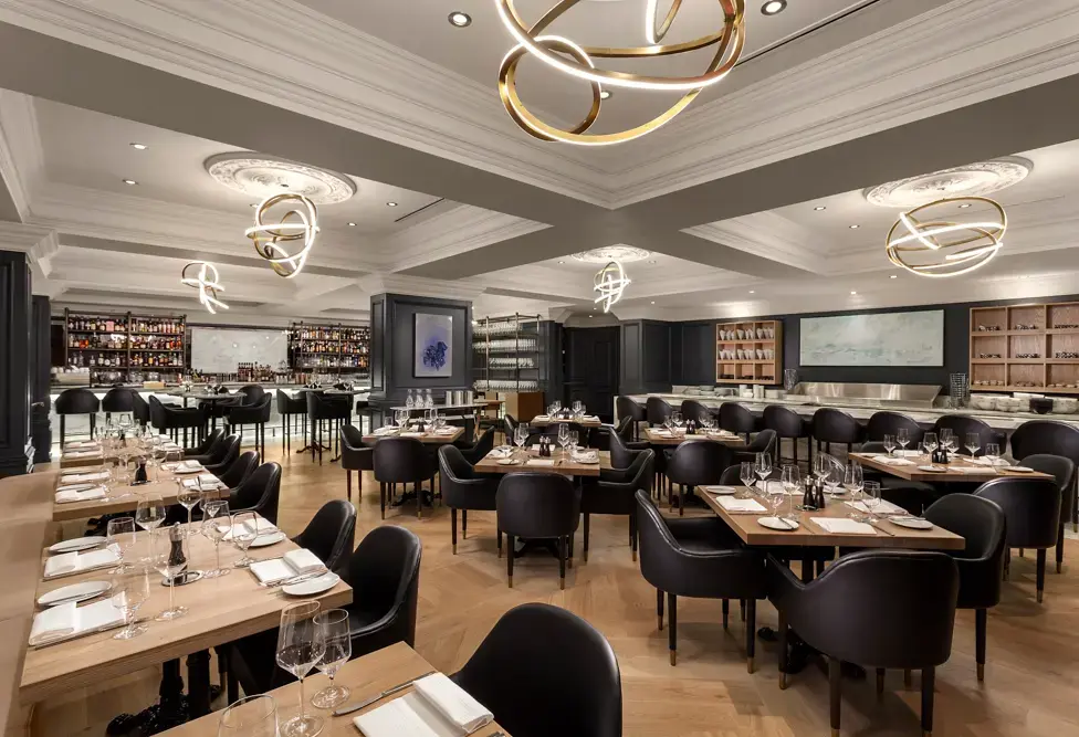 Modern restaurant interior with wooden tables, black chairs, and artistic circular ceiling lights.