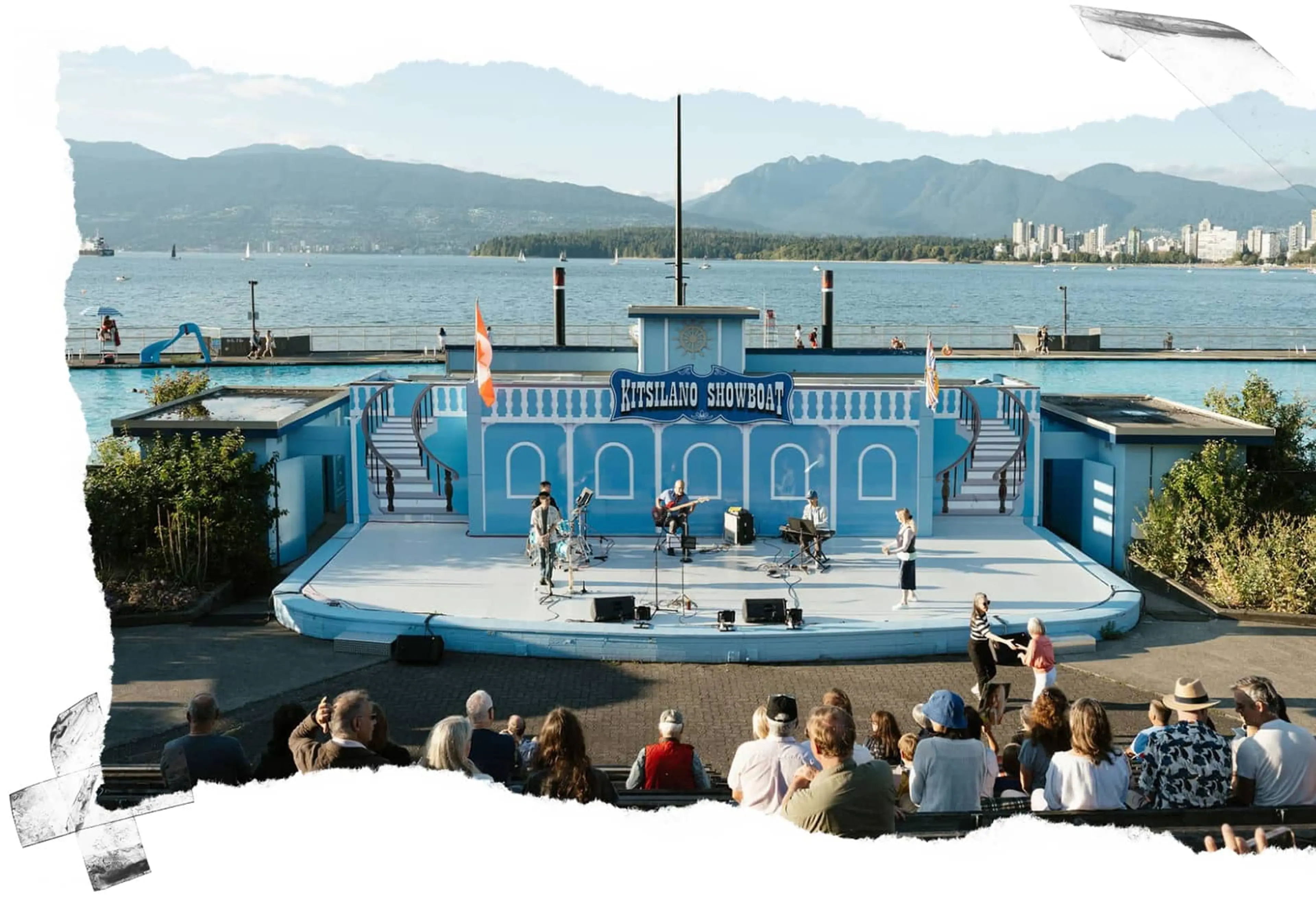 Outdoor stage with musicians performing at Kitsilano Showboat by the water, audience seated and two people dancing.