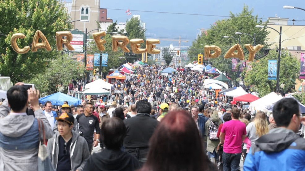 Crowded street festival with tents and booths, balloons spelling out Car Free Day overhead.