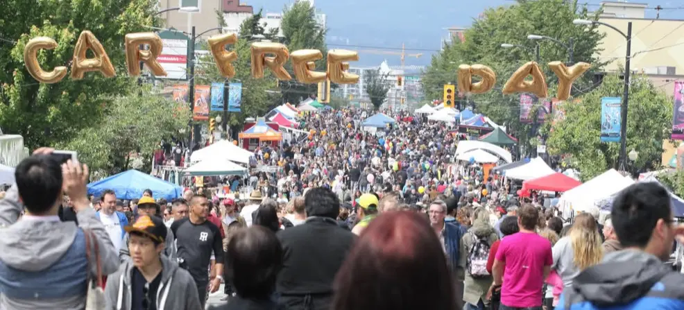 Crowded street festival with tents and booths, balloons spelling out Car Free Day overhead.