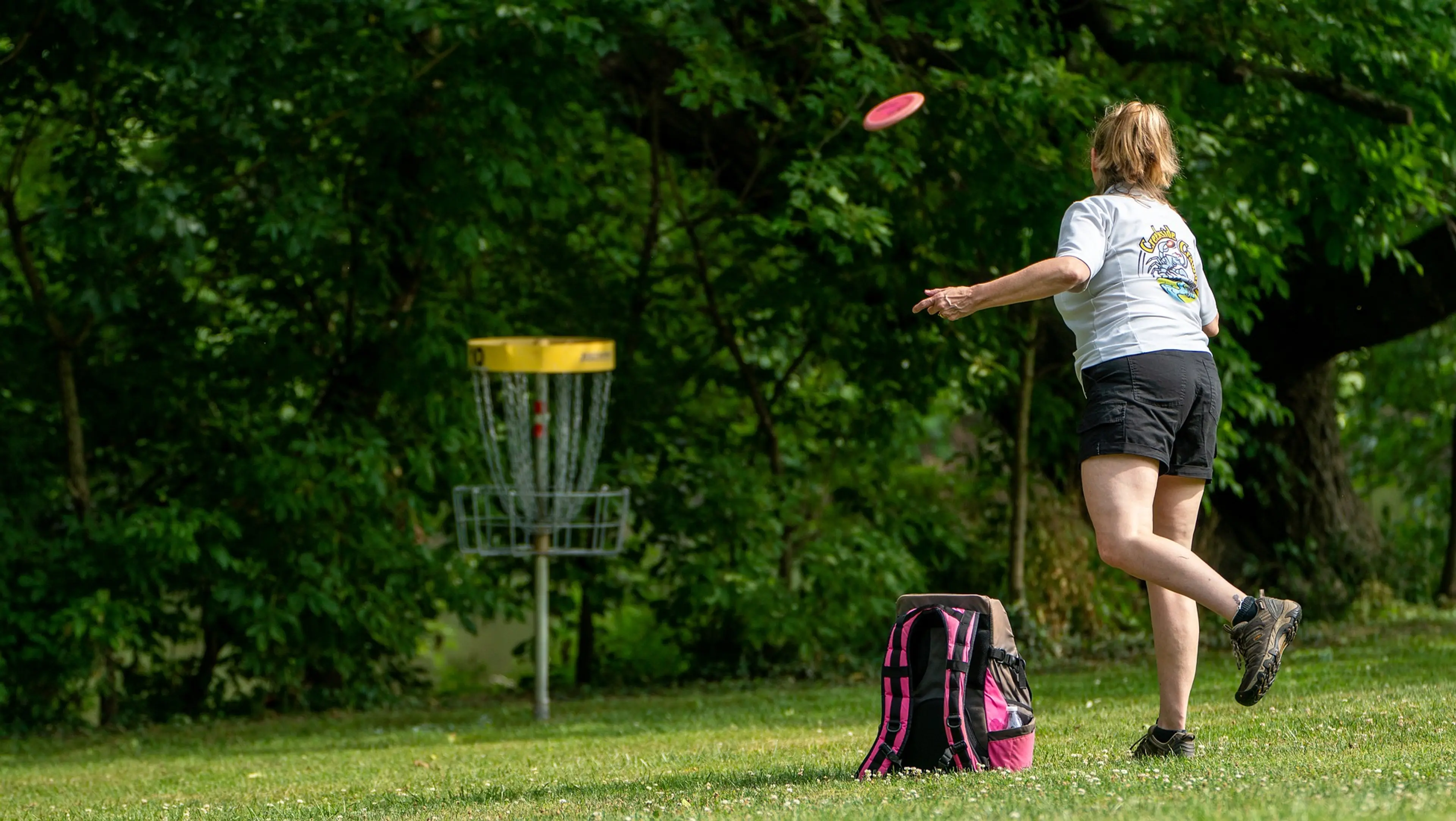 A woman throwing a disc at a disc golf basket