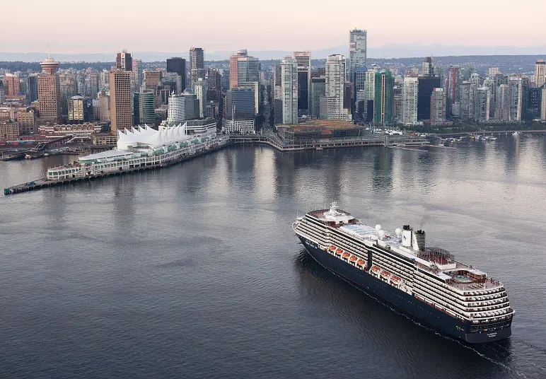 Large cruise ship sailing near a city skyline with tall buildings and a waterfront pier.