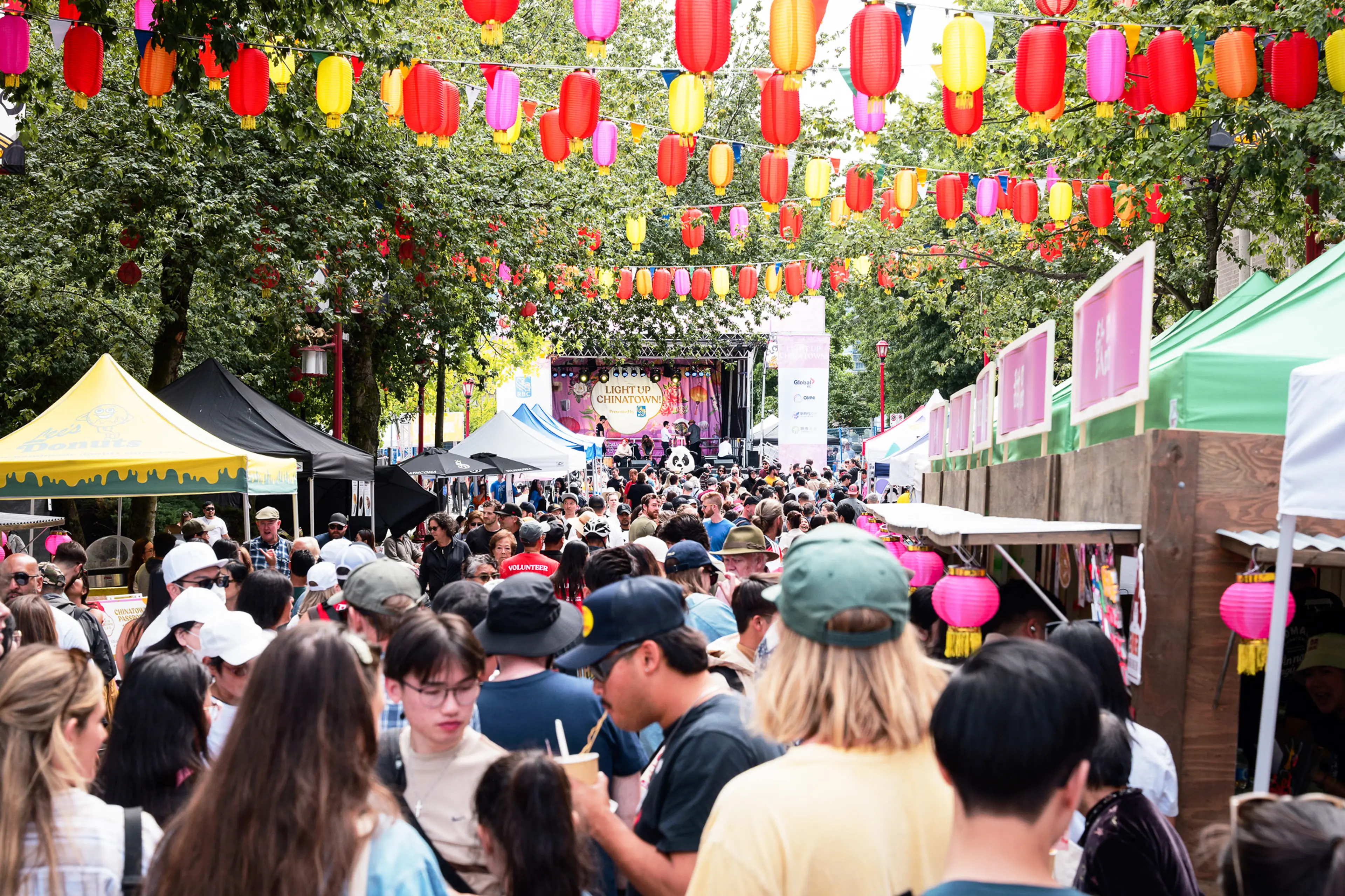 Crowded outdoor market with colorful lanterns hanging overhead and people walking among vendor tents.