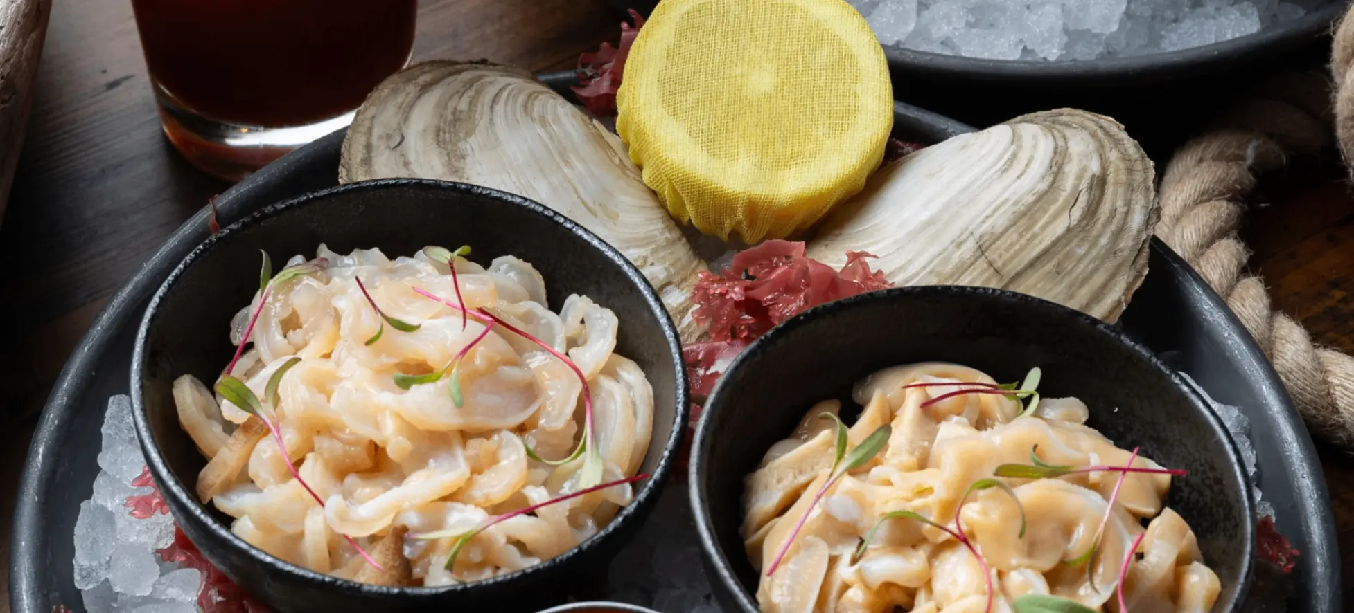 Seafood platter with two bowls of shellfish salad, three dipping sauces, lemon slice, and a cocktail garnished with an oyster and lemon wedge.
