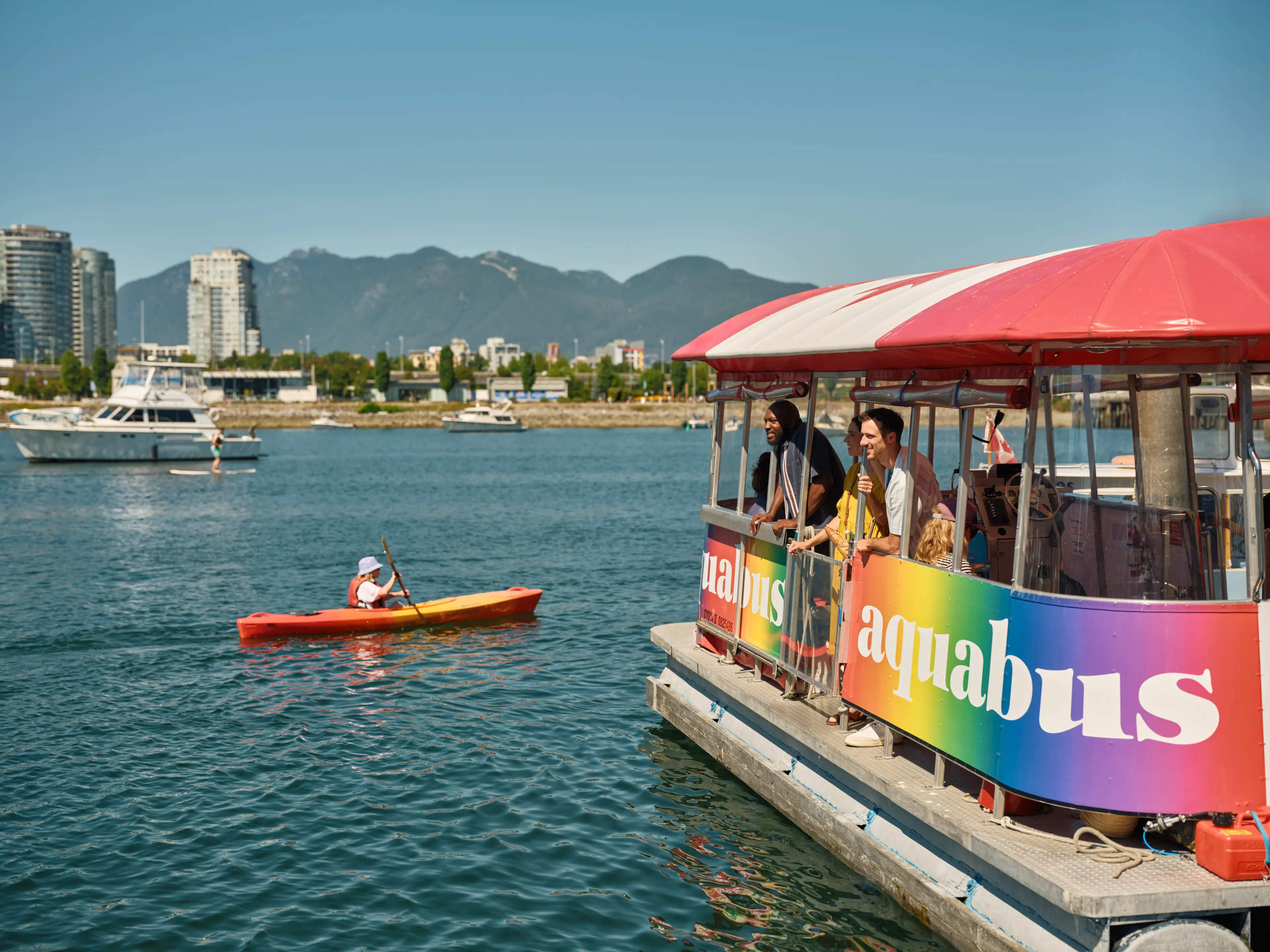 Aquabus and kayaker on the water in Vancouver during summer, with mountains in the background.