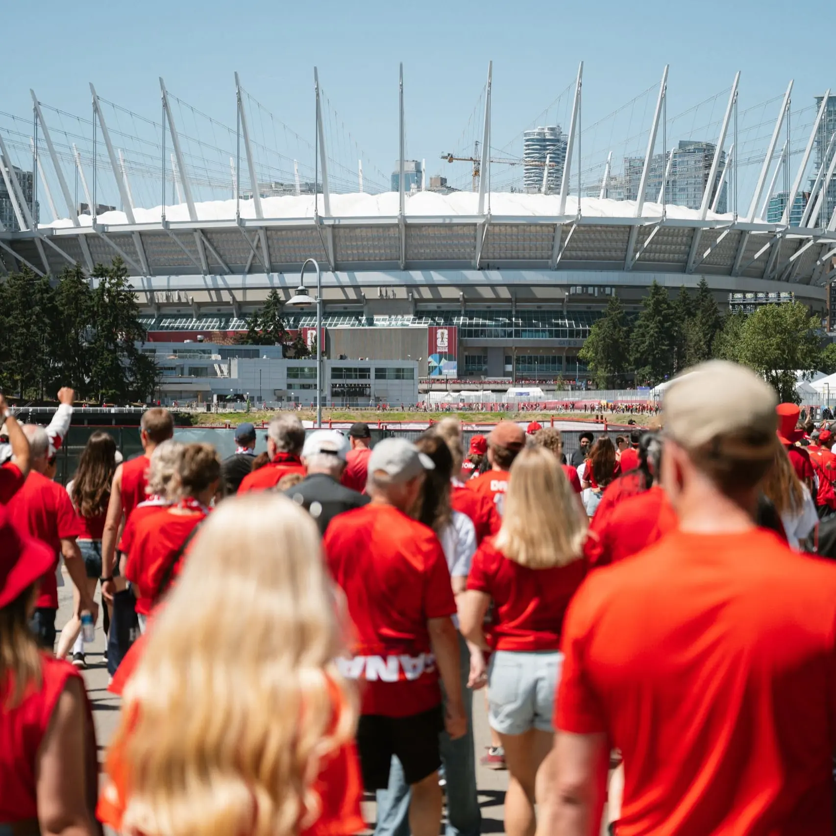 Crowd of people wearing red walking toward a large stadium with tall white spires on a sunny day.
