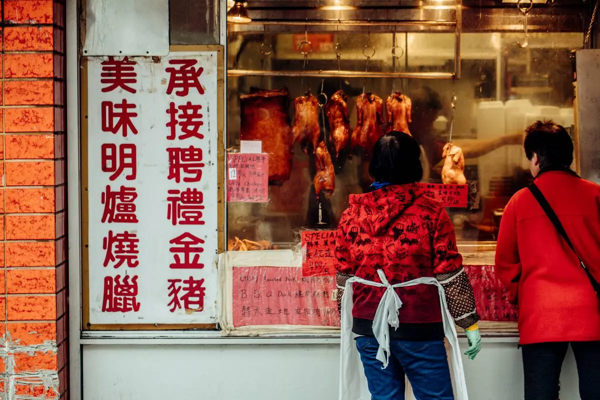 Customers look at BBQ meat in a Chinatown shop window