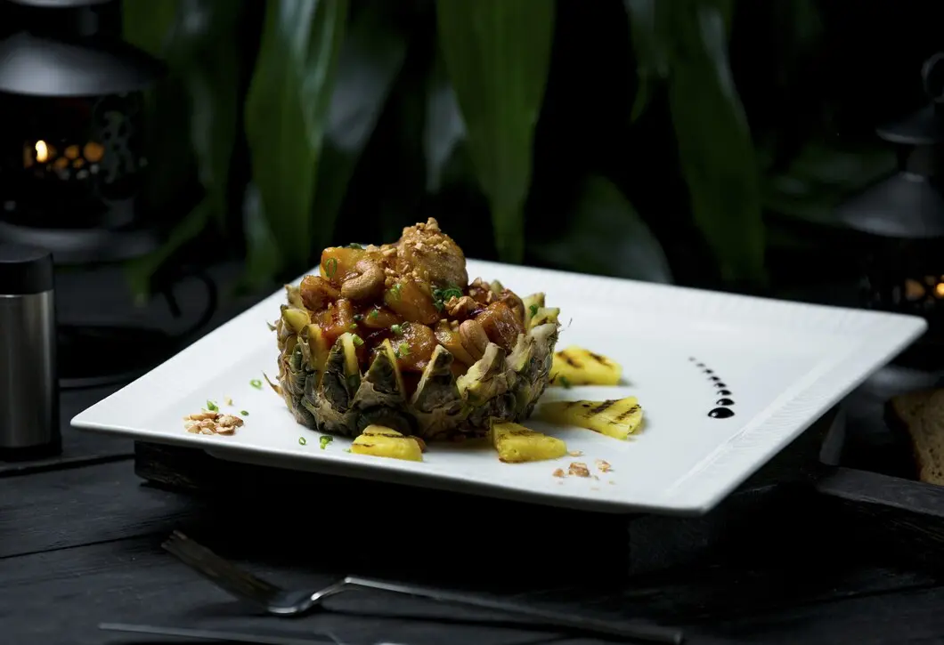 An exceptionally plated gourmet meal with pineapple and cashews on a white plate