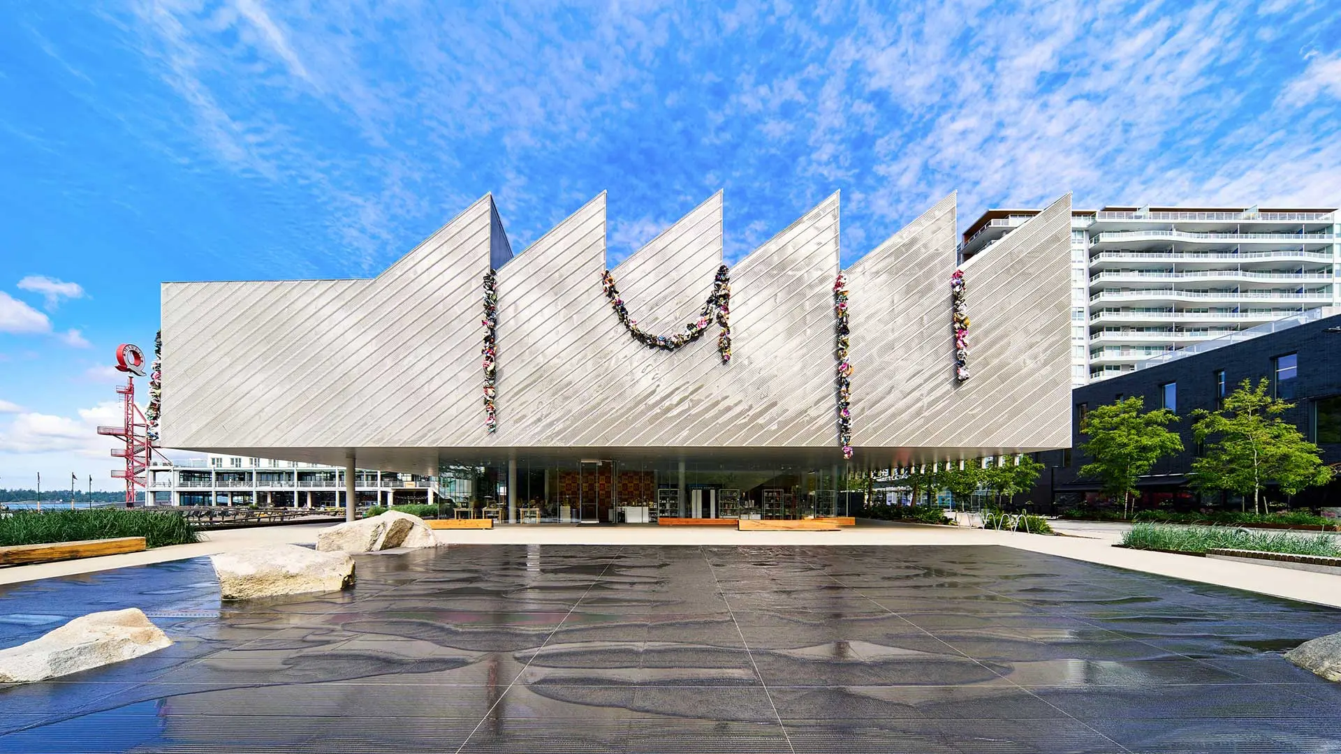 Modern architectural building with a distinctive zigzag roof design, decorated with floral garlands, set against a blue sky.