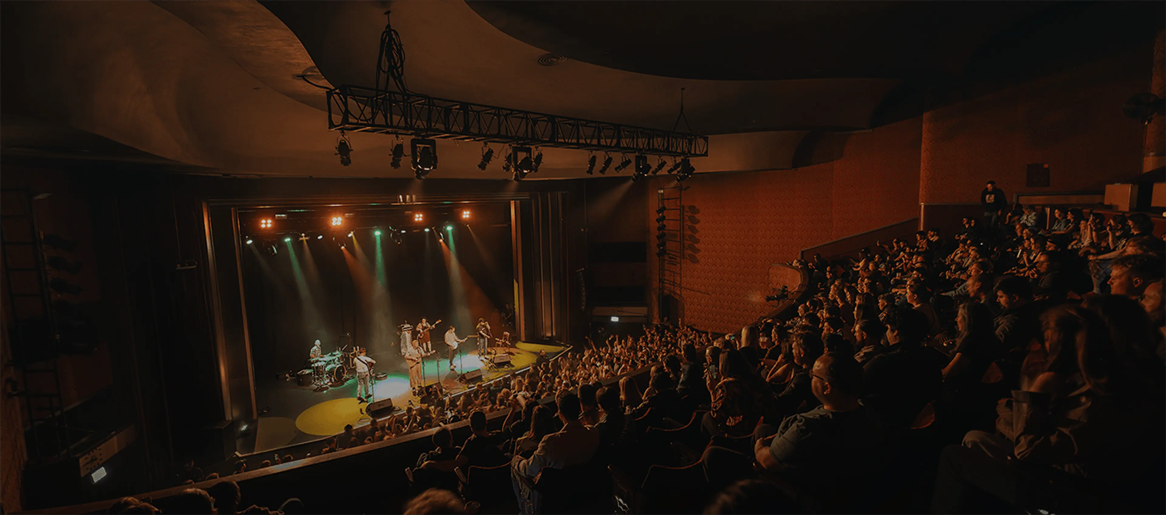 People watching a concert in a spacious auditorium, with bright lights and a performer on stage.