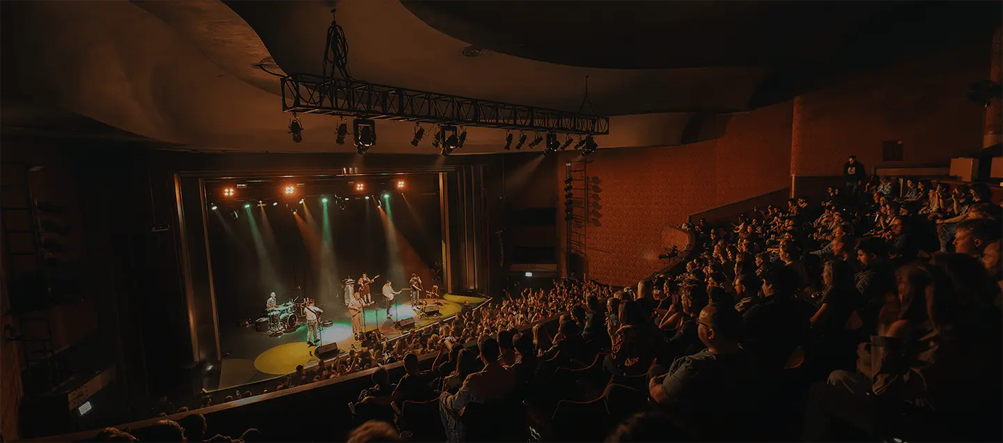 People watching a concert in a spacious auditorium, with bright lights and a performer on stage.