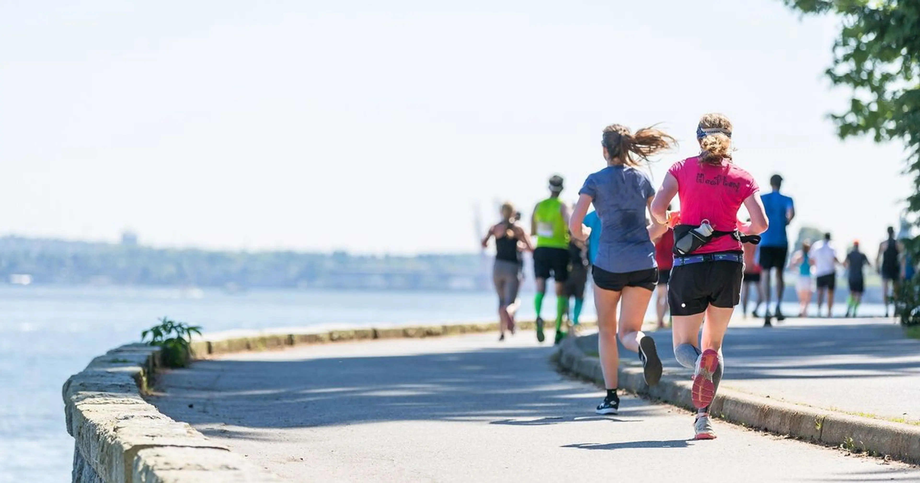 People running on a paved path along a waterfront on a sunny day.