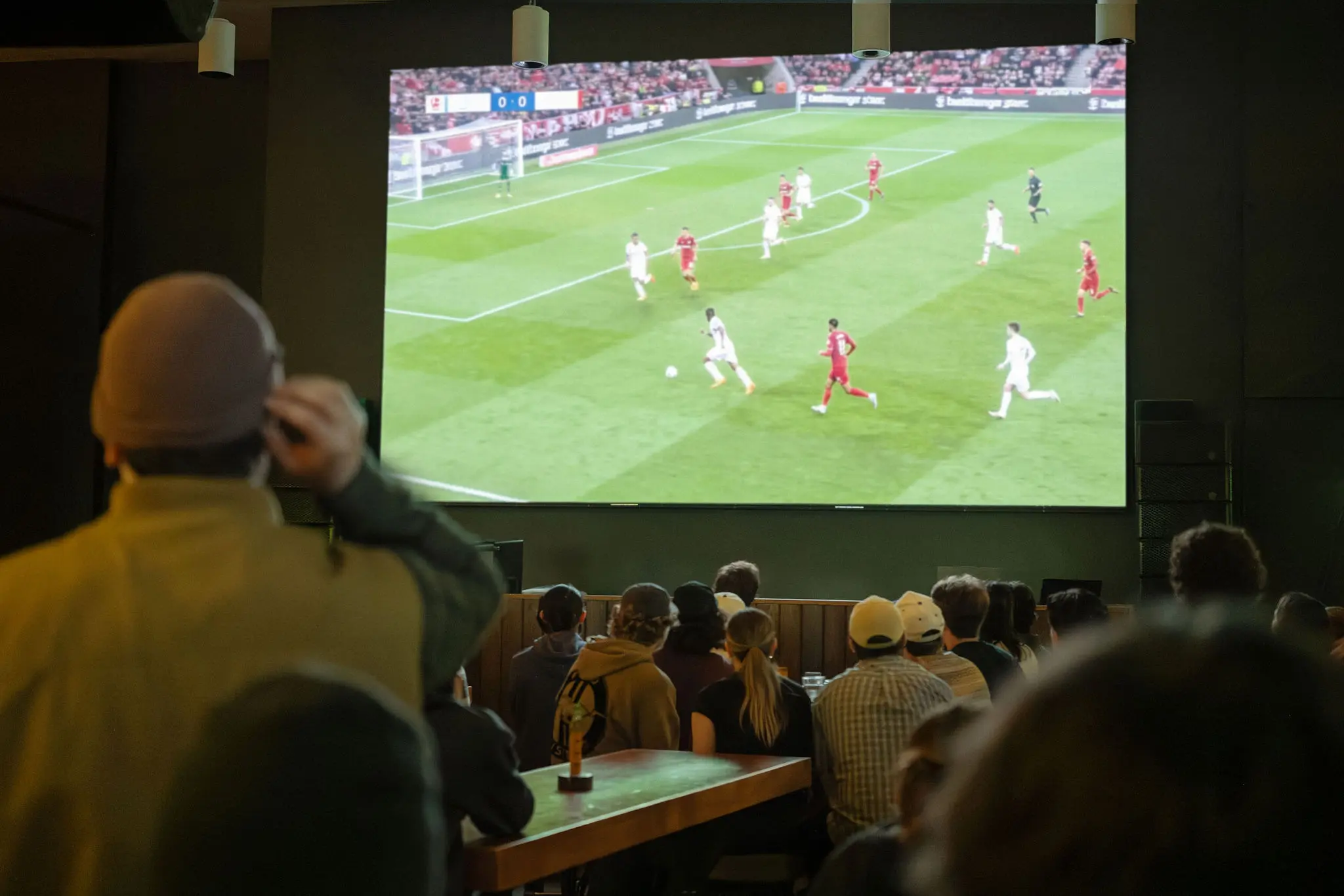 A group of people watching a soccer match on a large screen in a dark room.