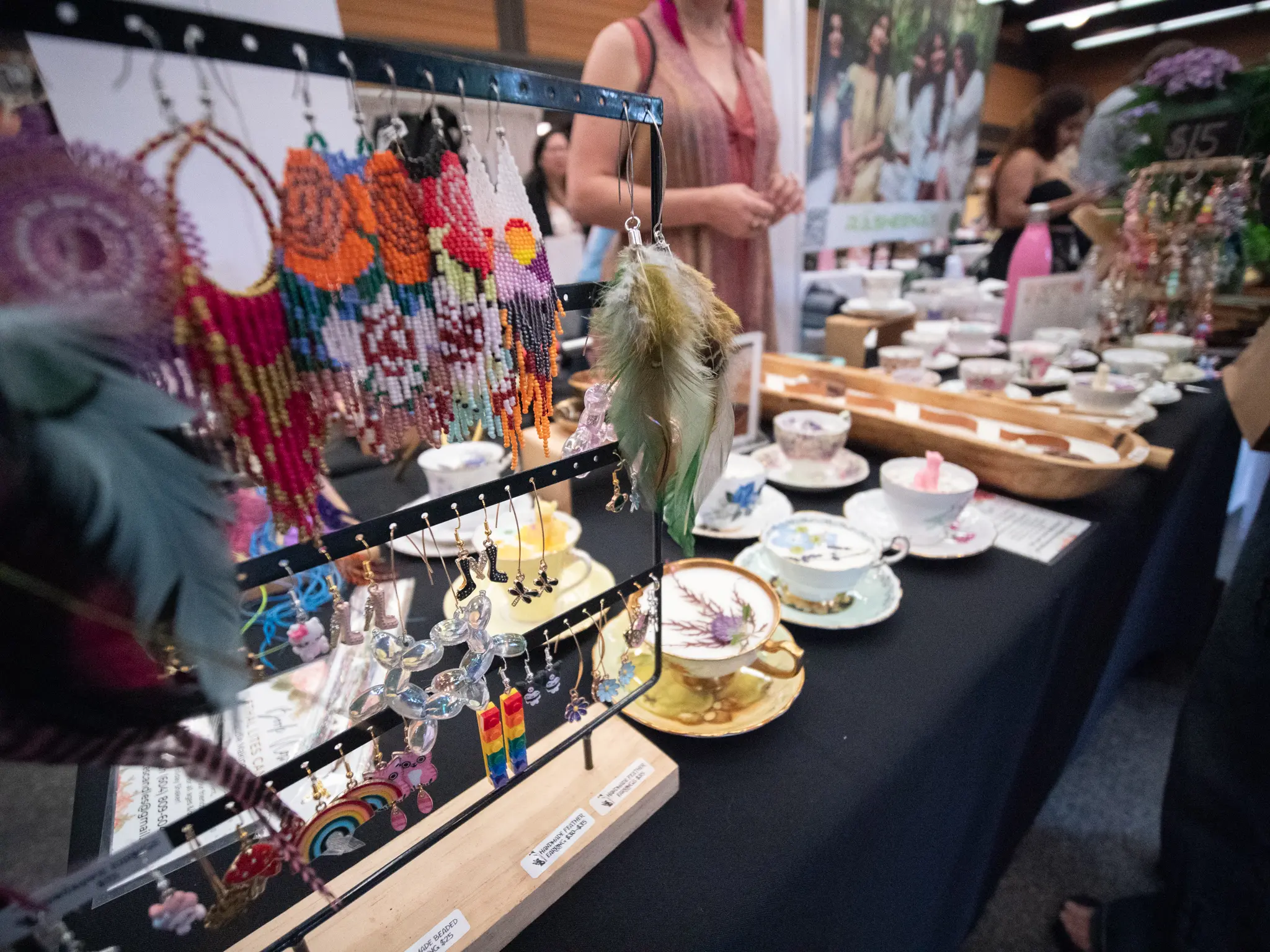 Colorful handmade earrings displayed on a rack with teacups and saucers on a table in the background at the Portobello West market..