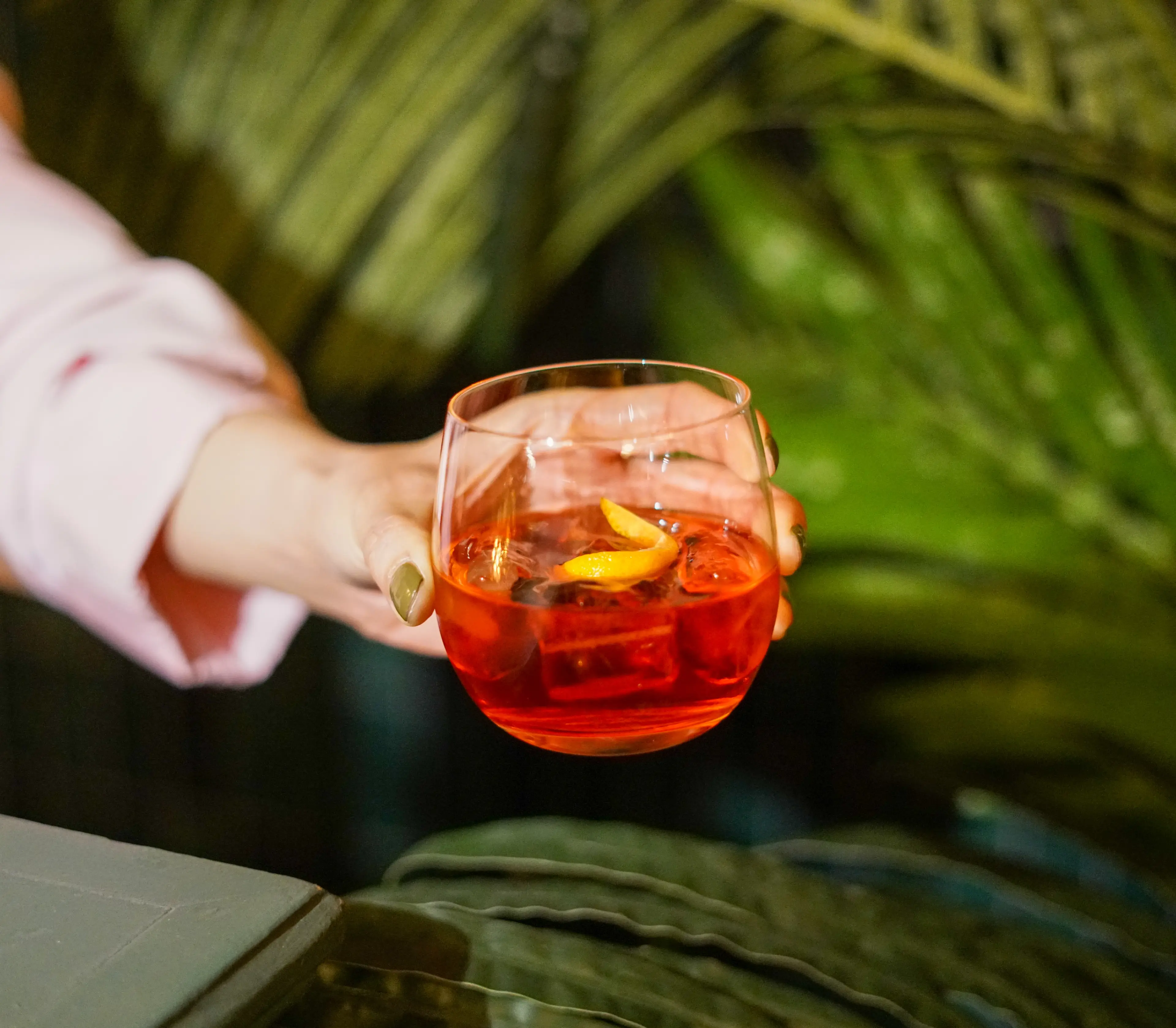Holding a drink in front of greenery during Vancouver Cocktail Week