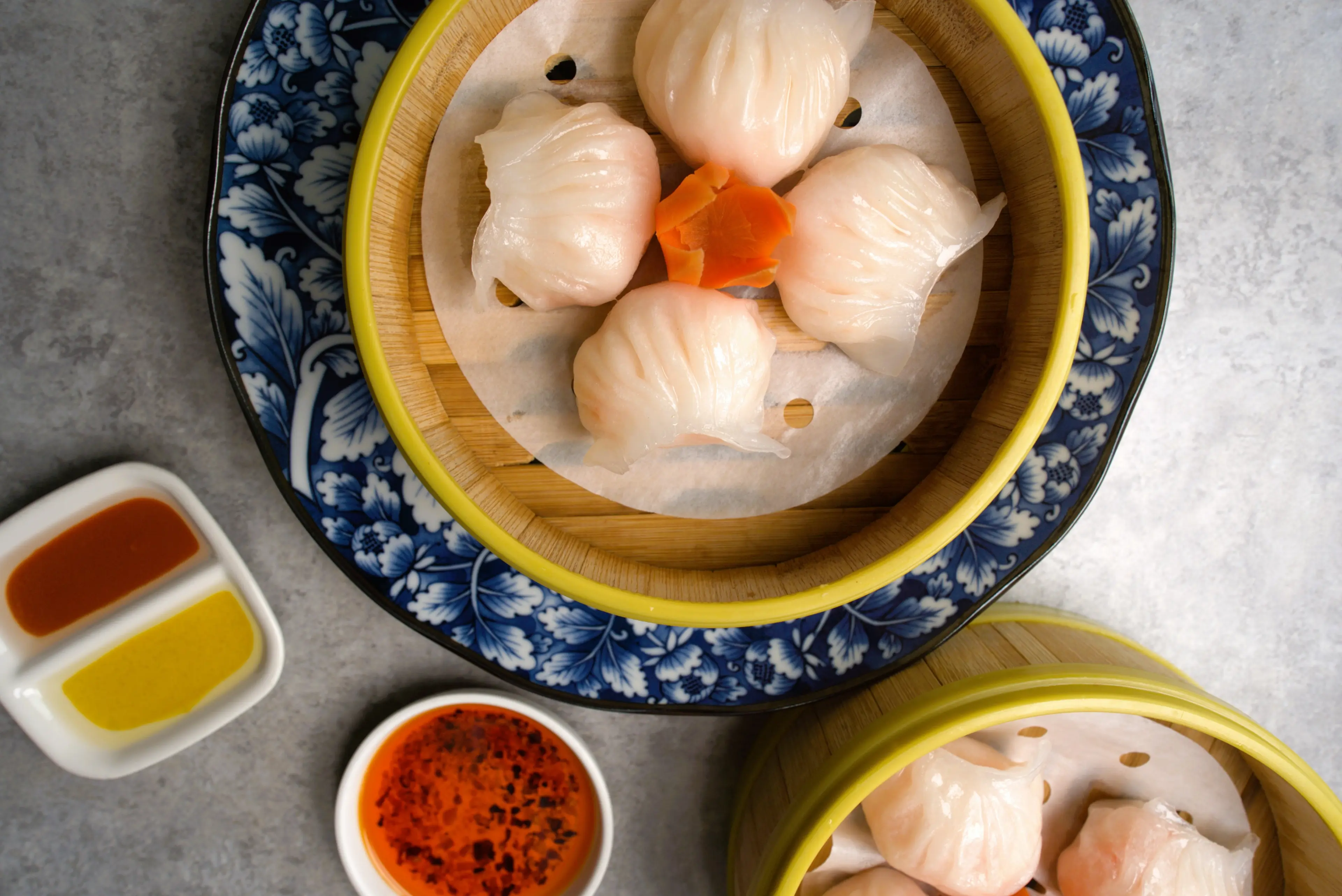 Four steamed dumplings in a bamboo steamer with dipping sauces on the side.
