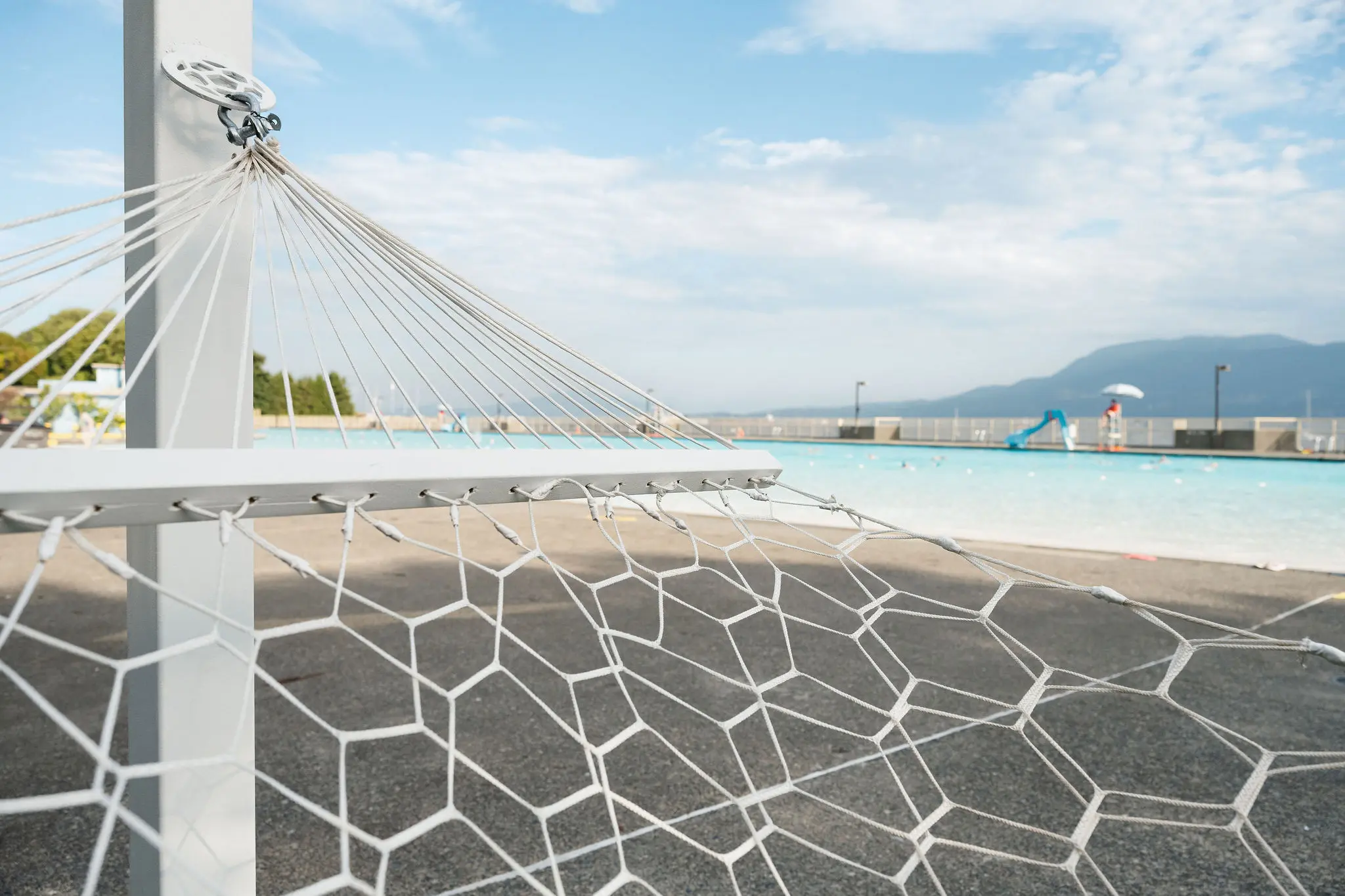 Close-up of a hammock tied to a post near an outdoor swimming pool with mountains in the background.