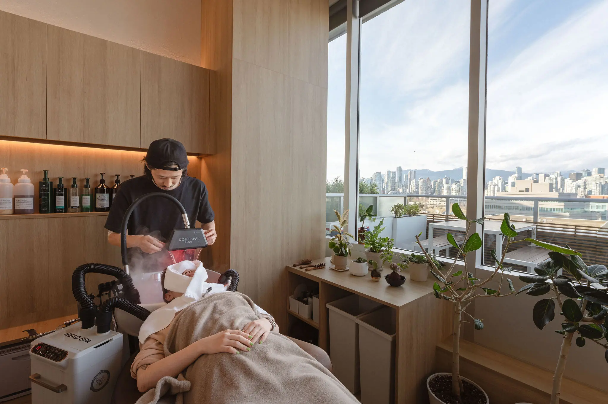 Interior of FORME Hair Salon & Head Spa with a client receiving a head spa treatment, salon window overlooking the North Shore Mountains.