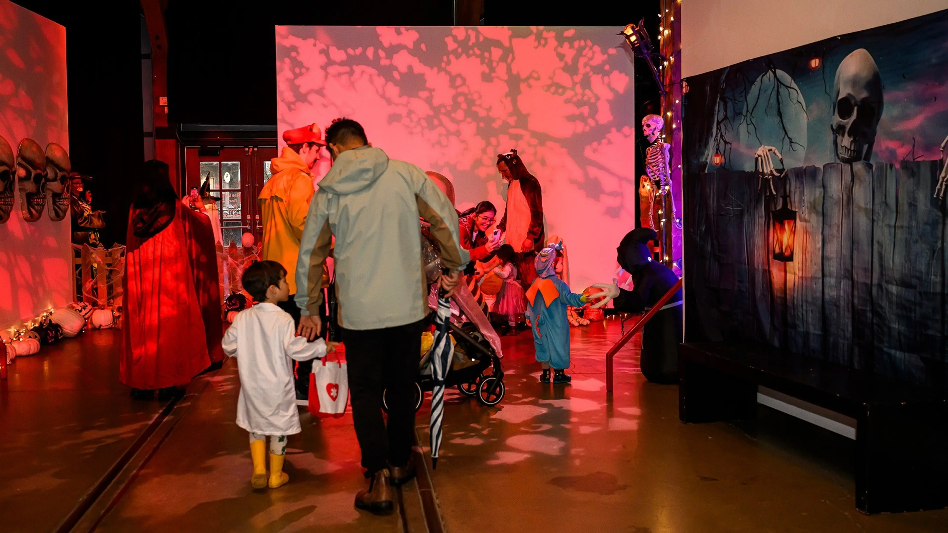 People in Halloween costumes walking and interacting in a dimly lit room with spooky decorations and red lighting.