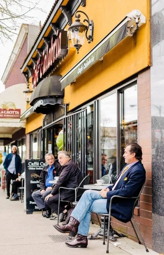 Customers are sitting and chatting at tables outside a small cafe