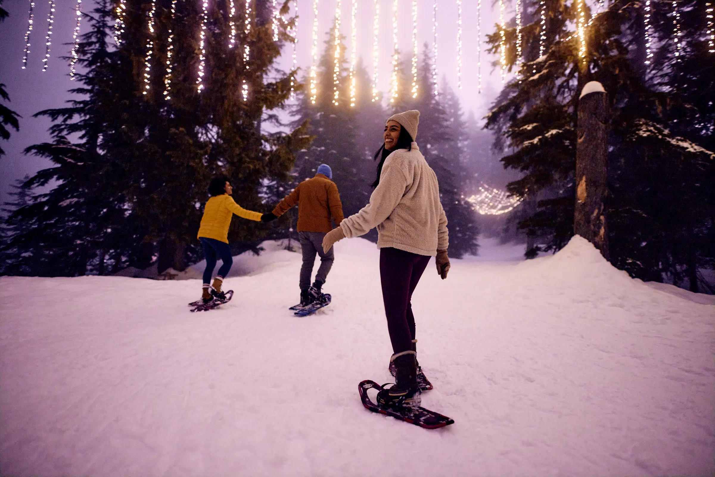 Three friends snowshoeing on Grouse Mountains on a trail with festive light installations.