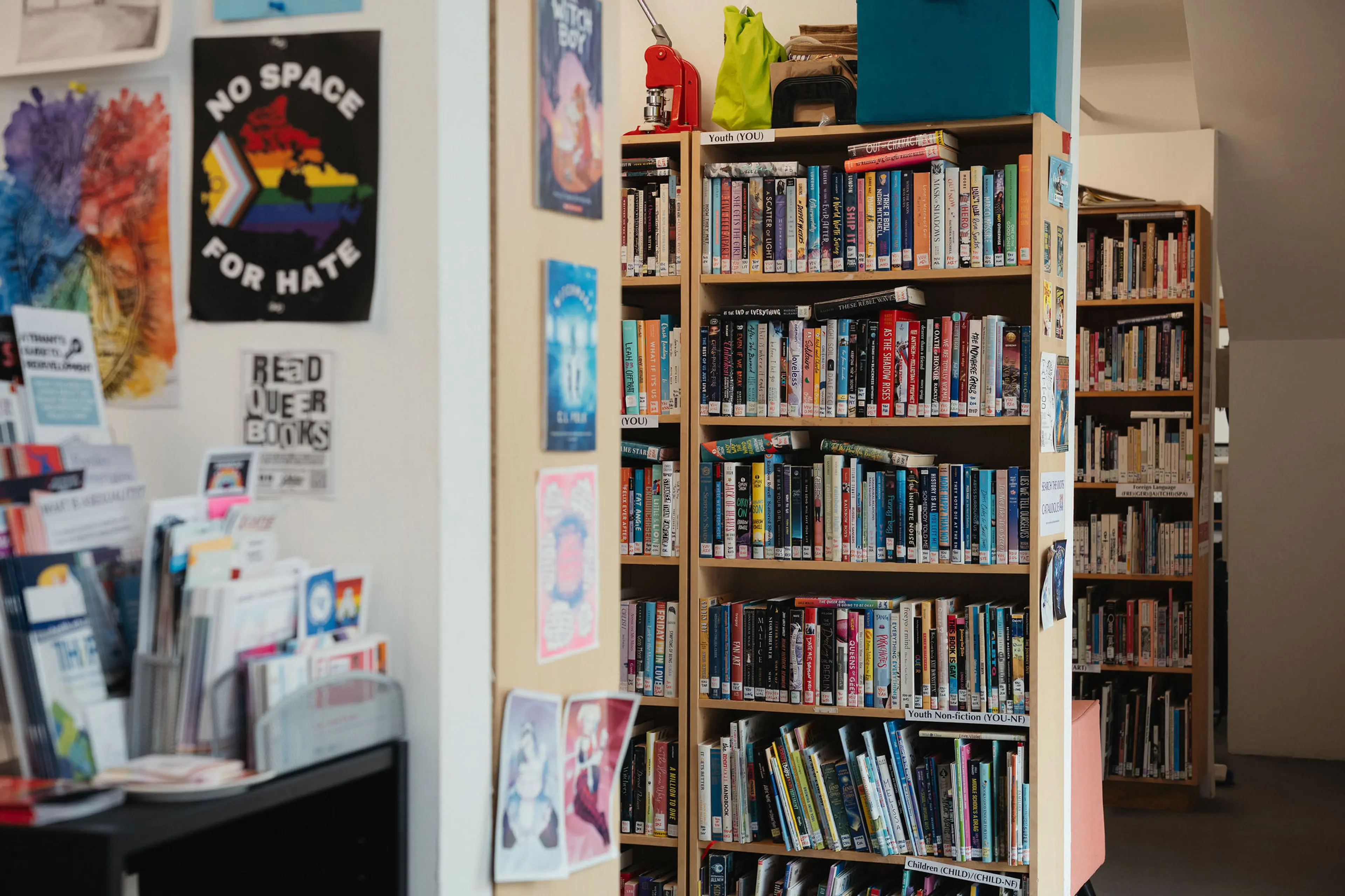 Bookshelves filled with books in a library corner, posters on the wall including one with a rainbow and text No Space for Hate.