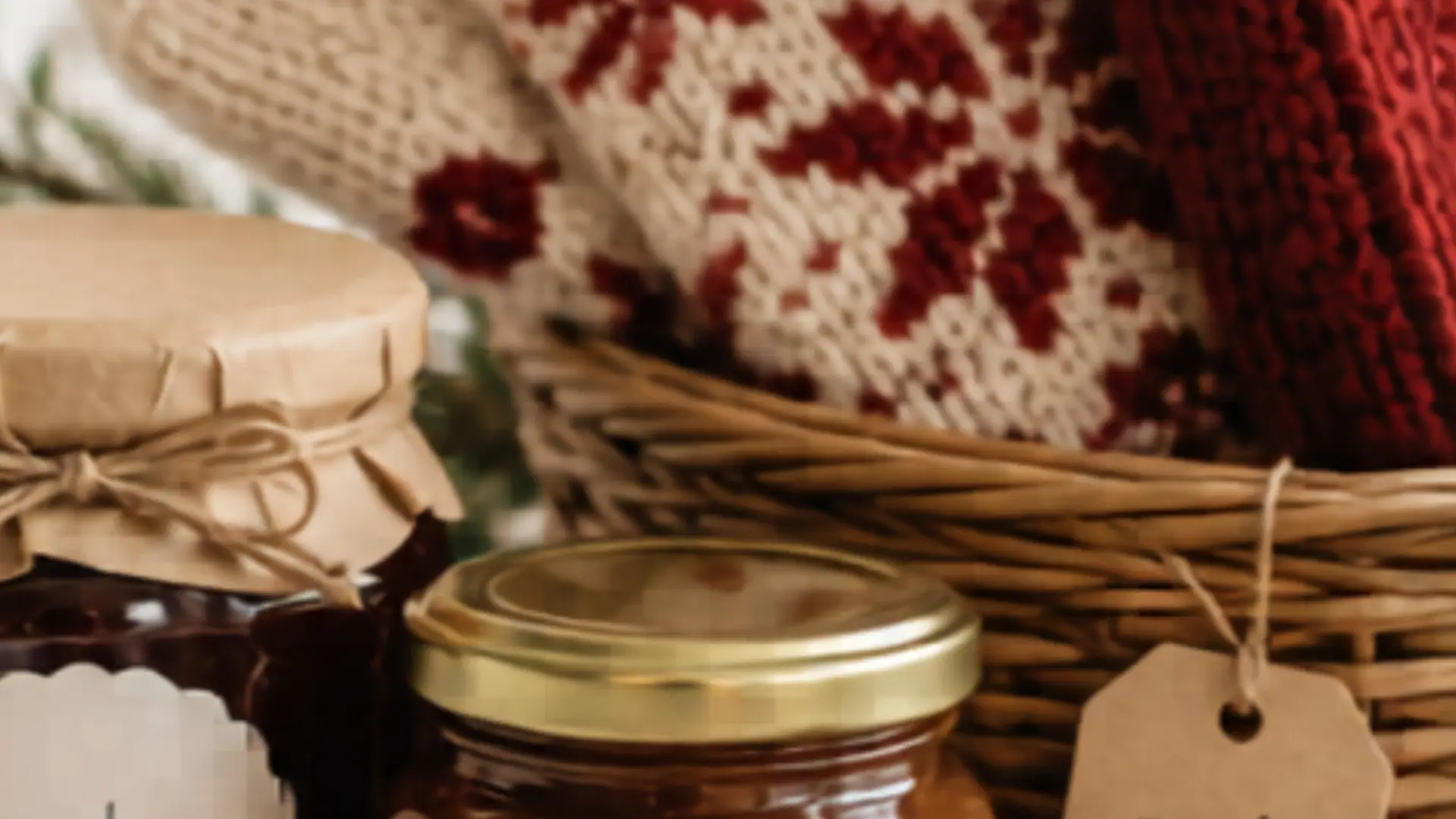 Two jars with brown and gold lids in front of a wicker basket holding red and beige knitted items with a floral pattern.