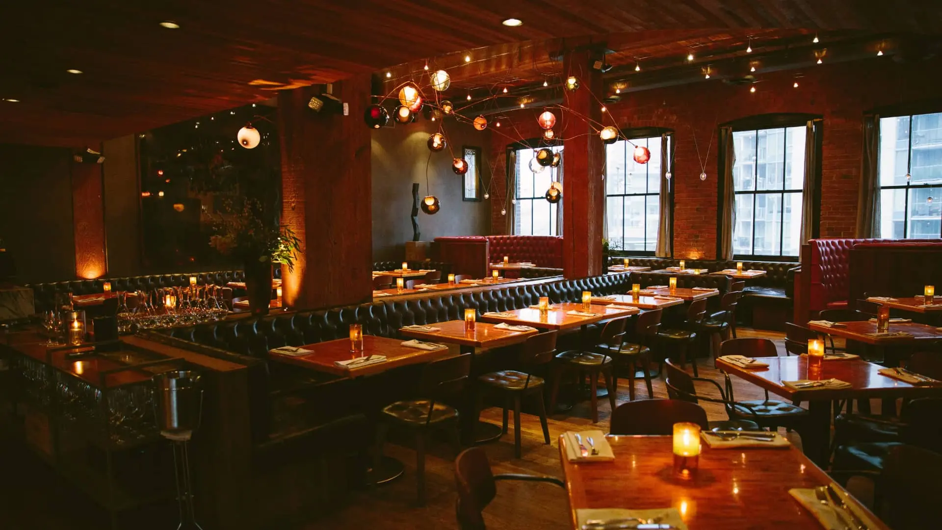 Dimly lit restaurant interior with wooden tables, black chairs, tufted leather booths, and hanging globe lights.