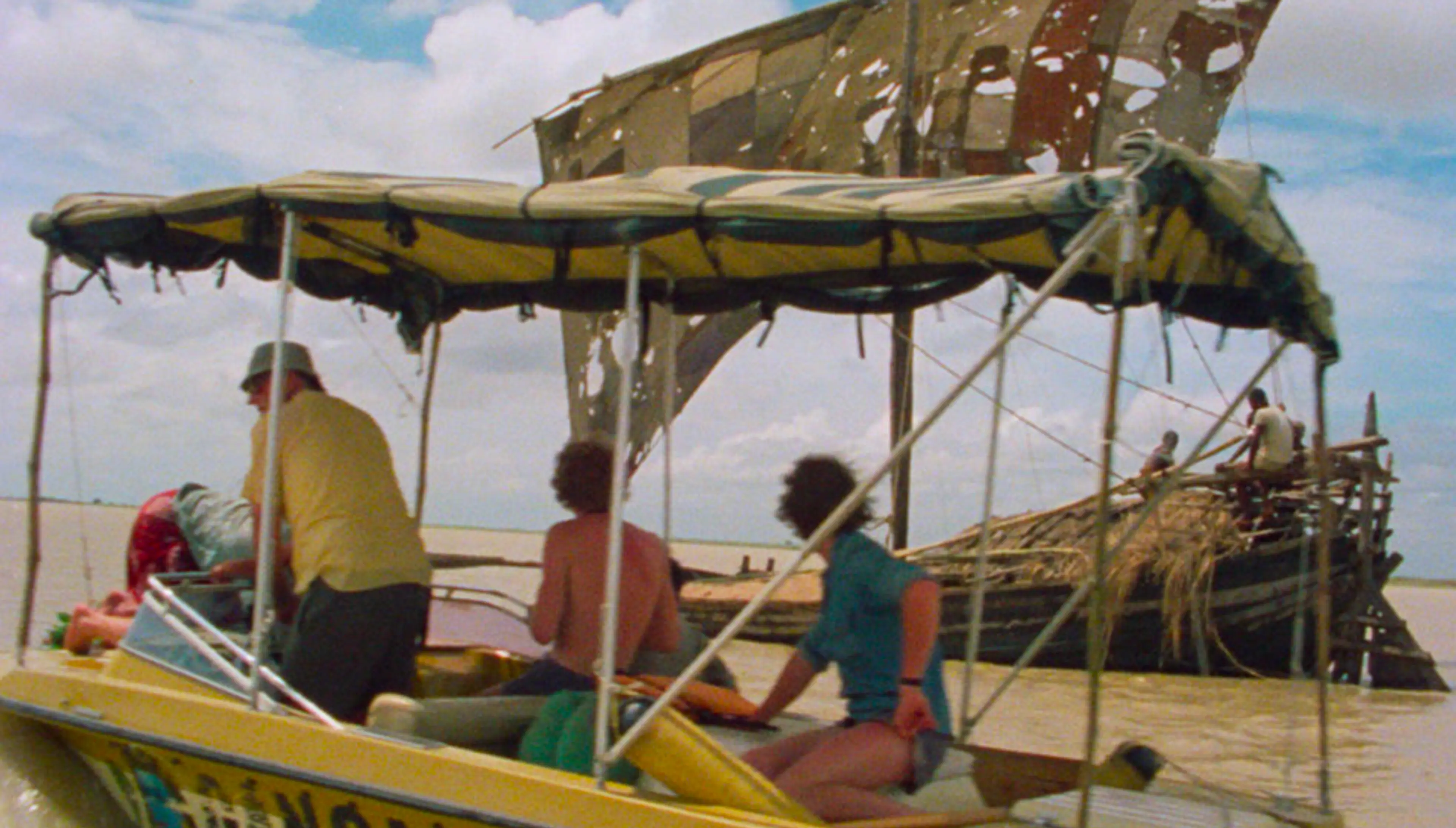 Men sit on a boat with a tattered canopy - still from the film Ocean to Sky