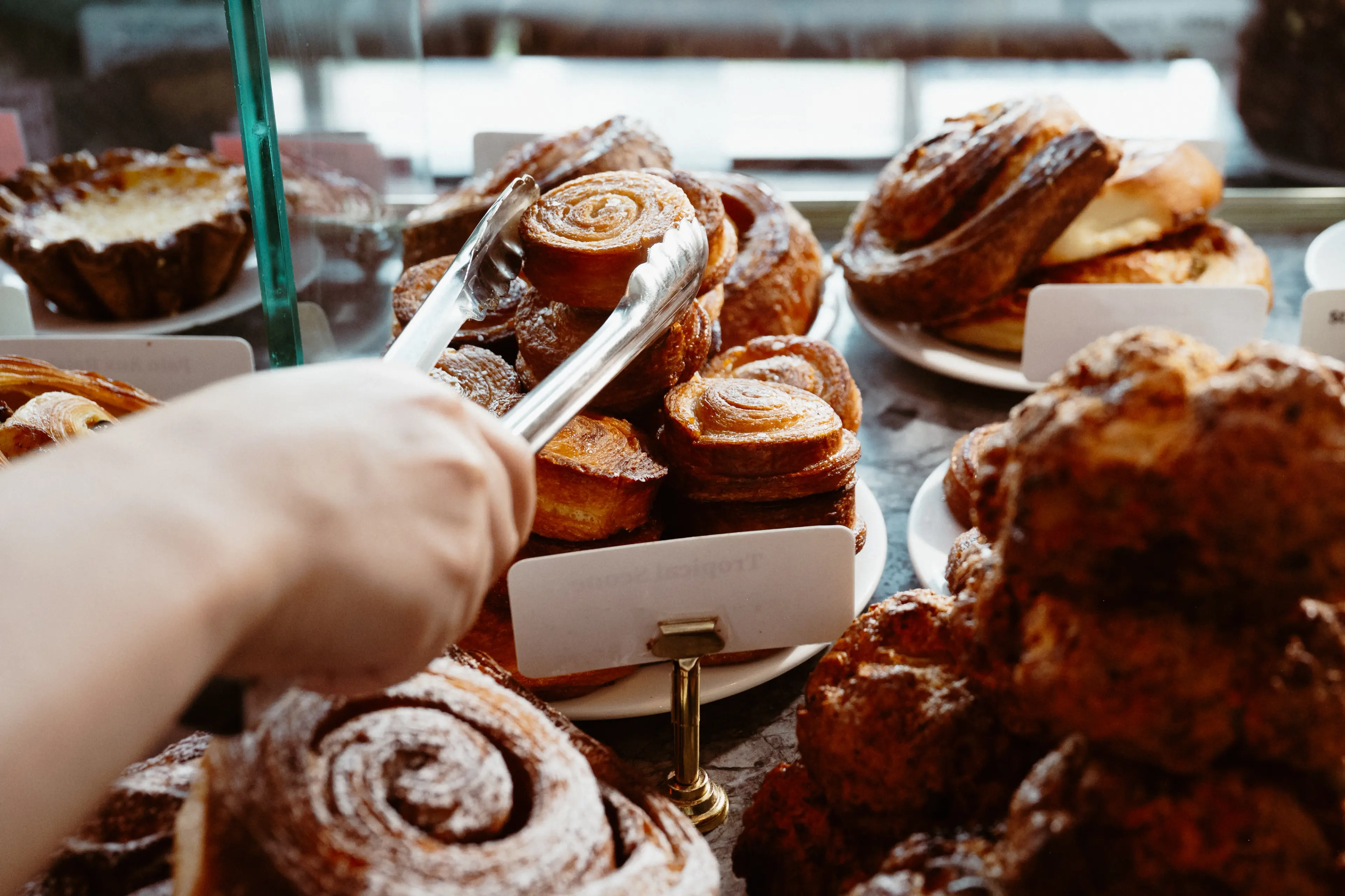 A display of baked goods with a hand using tongs to pick up a pastry.