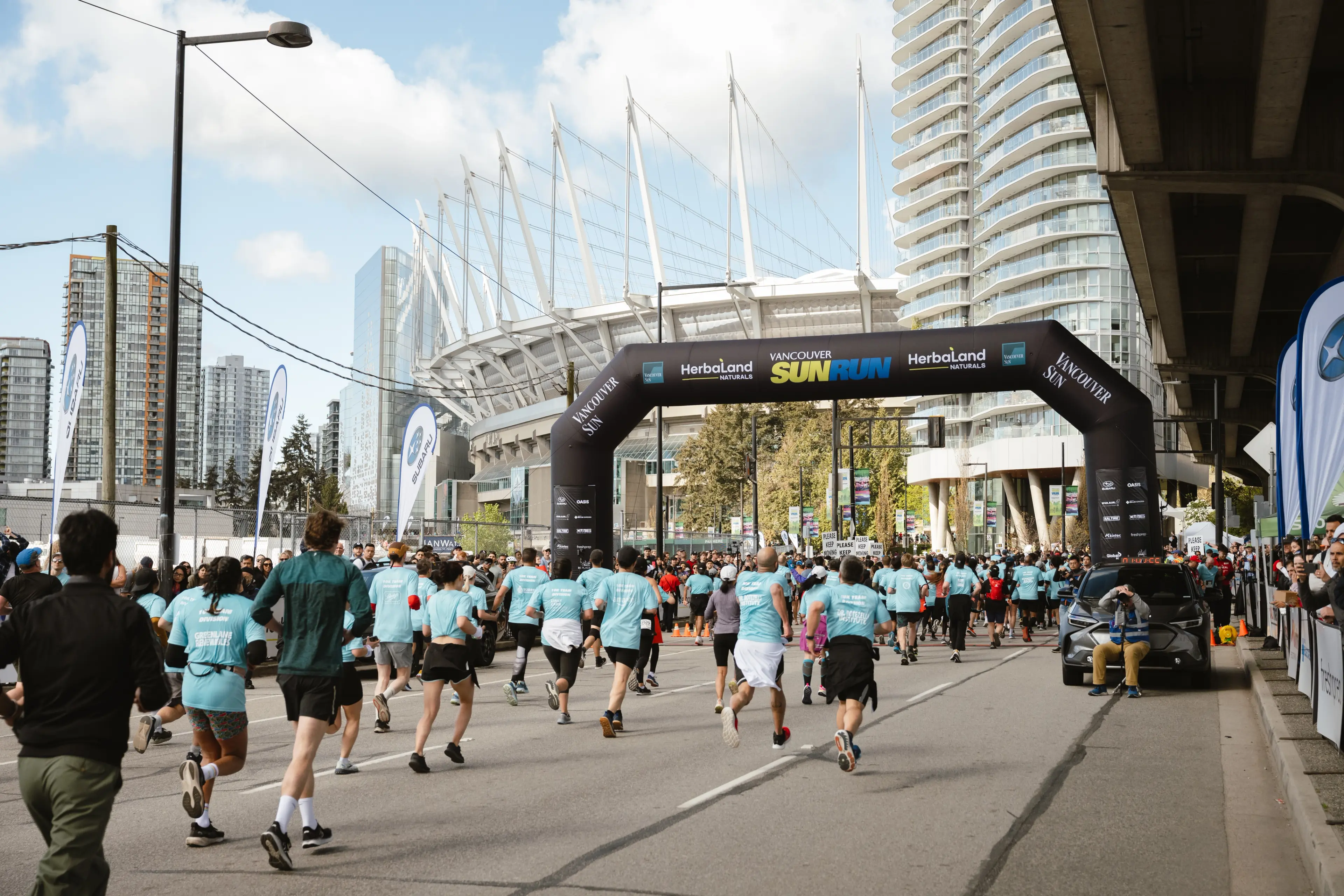 Runners running towards a Sun Run arch with BC Place in the background in Vancouver.
