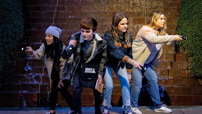 A group of four people pose with flashlights while playing a Vancouver Mysteries adventure game