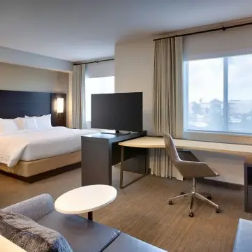 Hotel room with a large bed, TV on a stand, desk with chair, window with curtains, and a small round table next to a sofa.