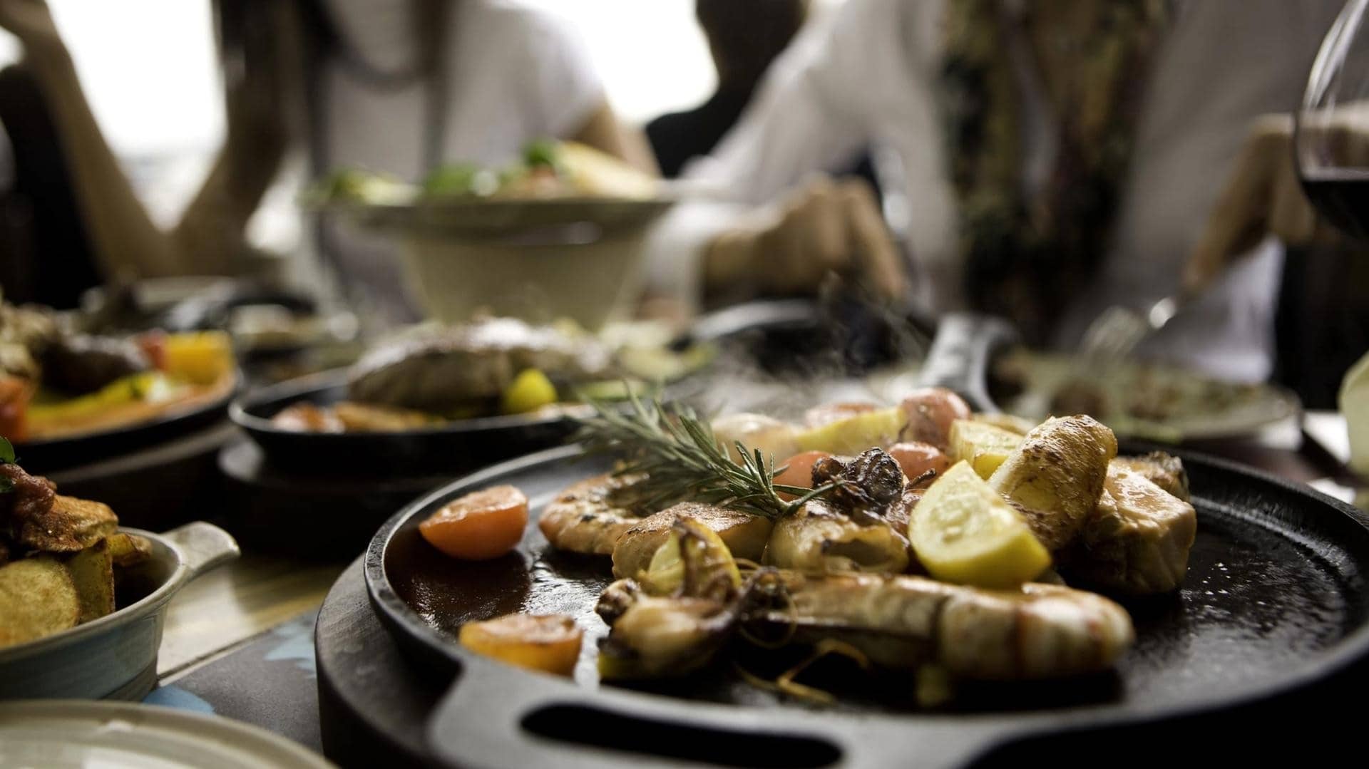 Sharable seafood with lemon and garnish is being served on hot plates in a restaurant