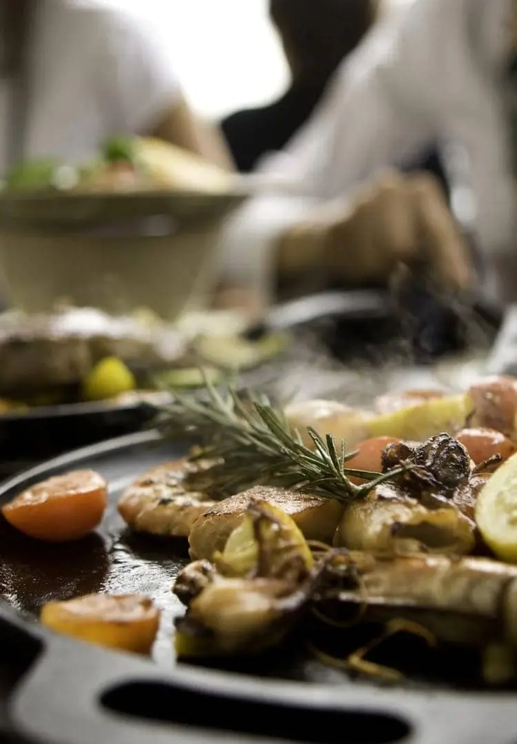 Sharable seafood with lemon and garnish is being served on hot plates in a restaurant