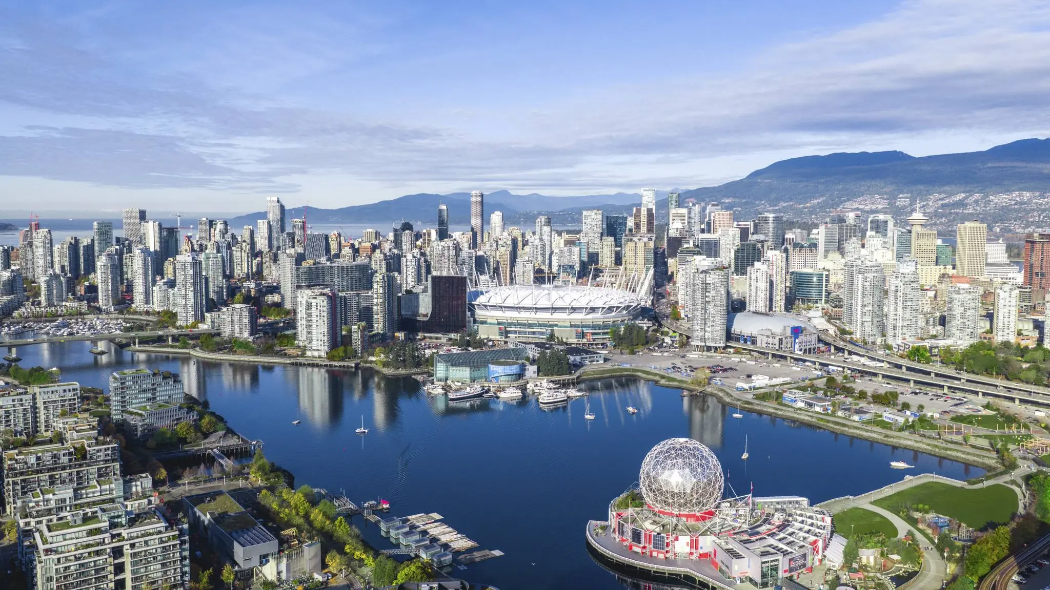Aerial view of Vancouver city skyline with BC Place stadium waterfront, under a partly cloudy sky.