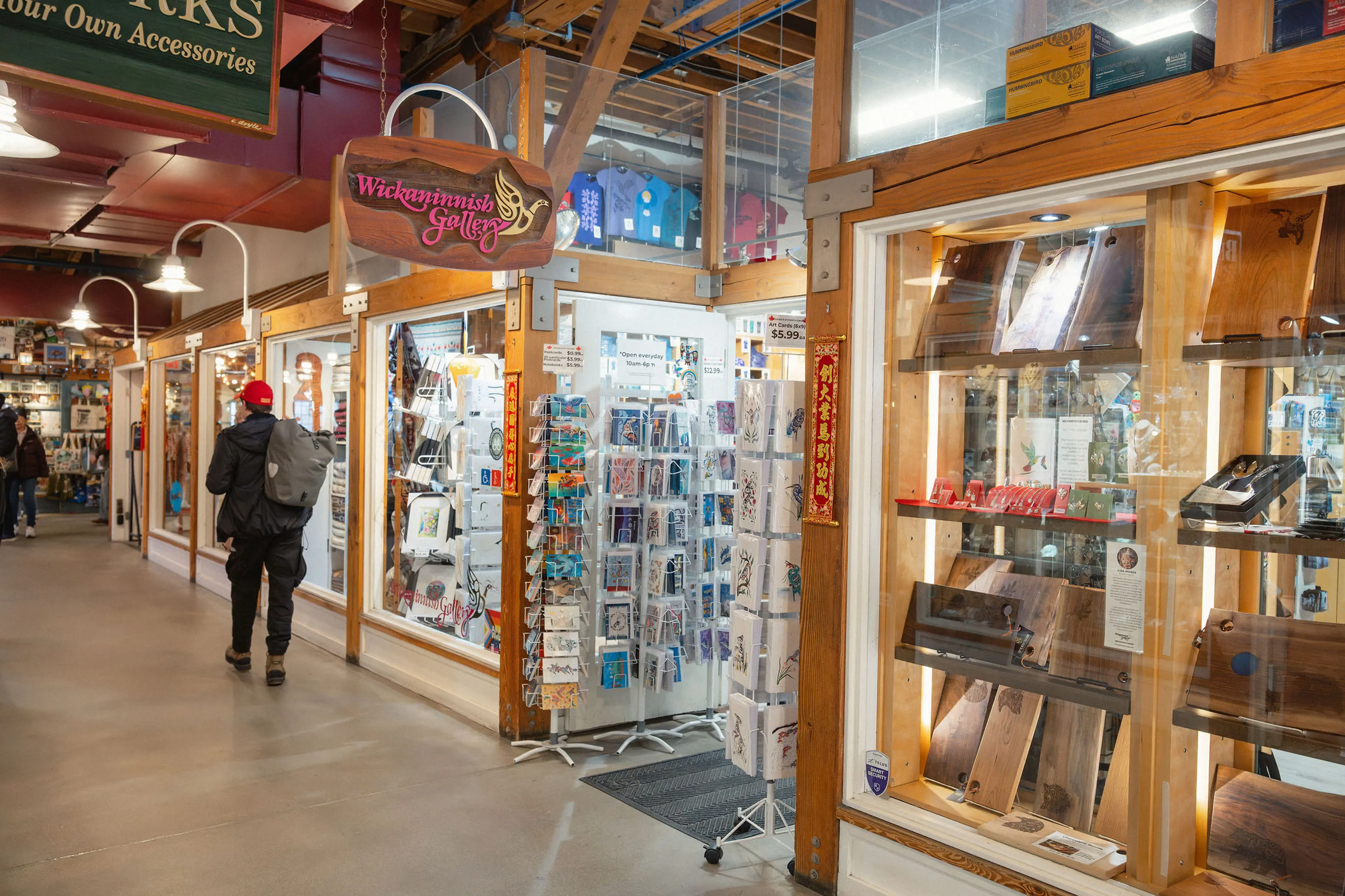 Person with backpack walking inside a market with wooden-framed glass display cases and a sign reading Wickaninnish Gallery.