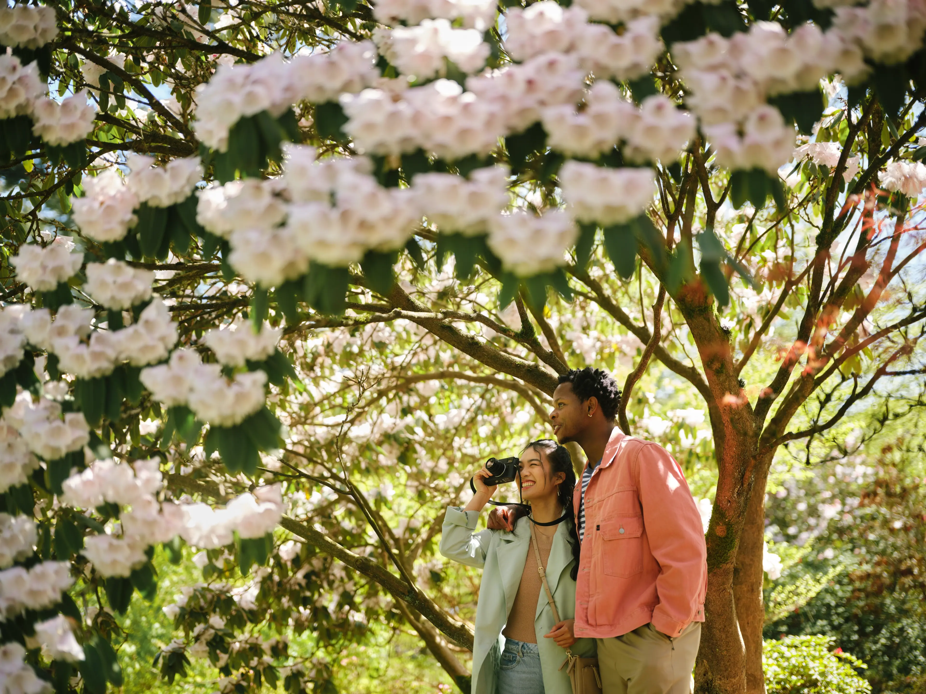 A woman stops to take a photo at VanDusen Botanical Garden with another person having their arms around them.