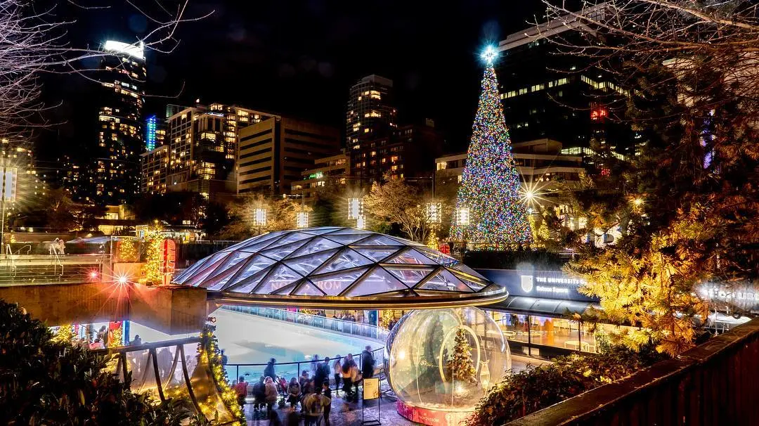 The outdoor ice rink at Robson Square in Vancouver lit up at night with holiday light displays on the nearby trees.