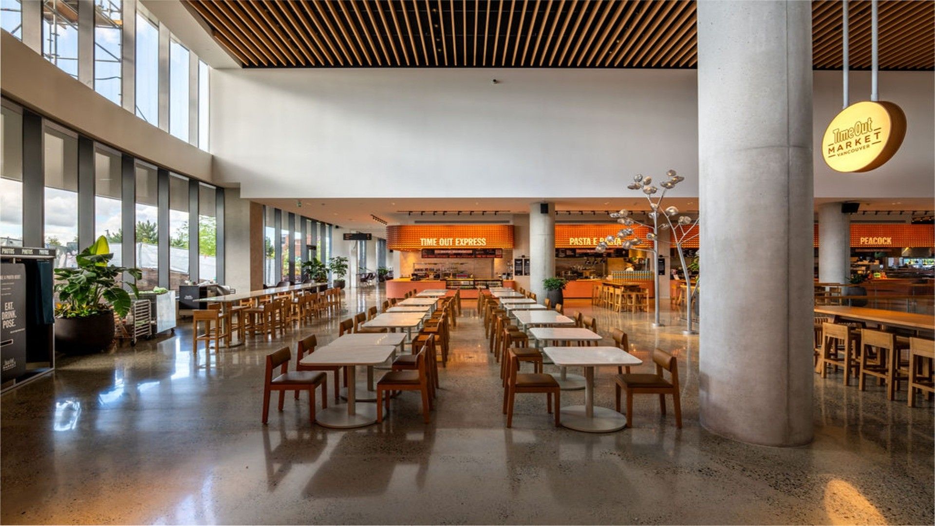 Empty modern food court with rows of tables and chairs, large windows, and illuminated food stall signs.